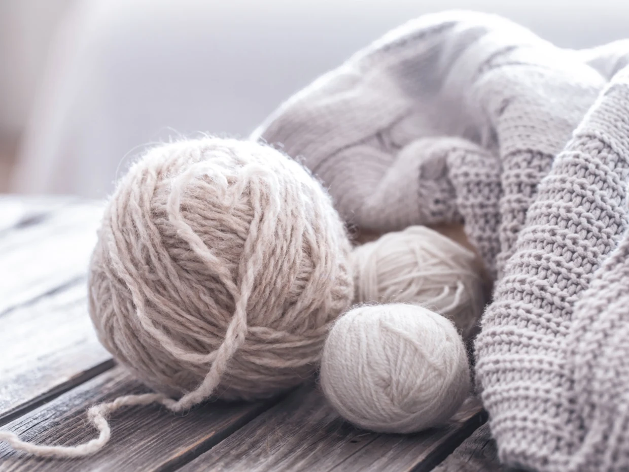 Beige Wollknäuel und gestrickter Pullover auf einem Holztisch. Beige Wollknäuel und gestrickter Pullover auf einem Holztisch.