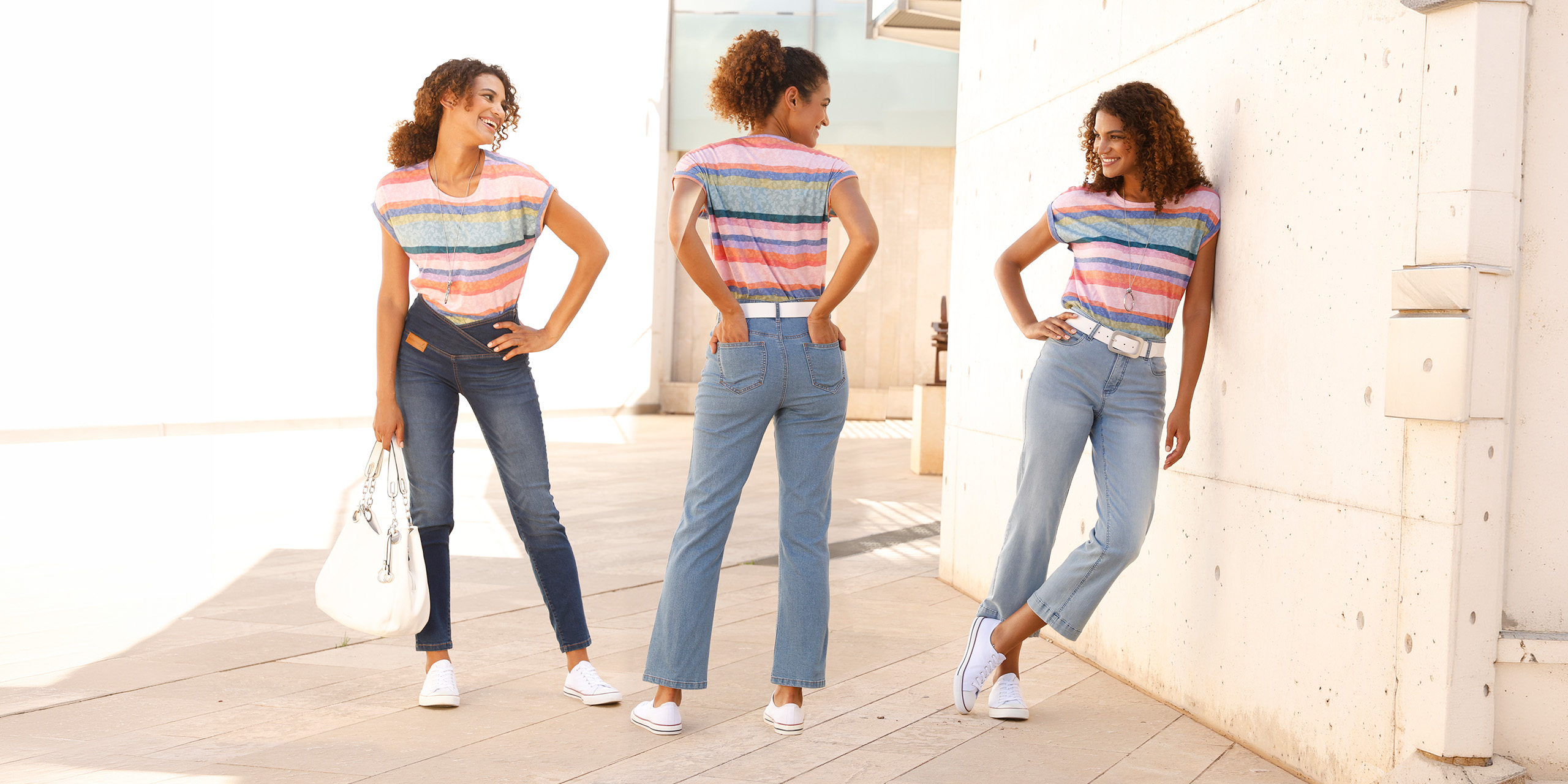 Drei Frauen in verschiedenen Jeansmodellen und bunt gestreiften T-Shirts posieren lächelnd im Freien vor einer hellen Wand.