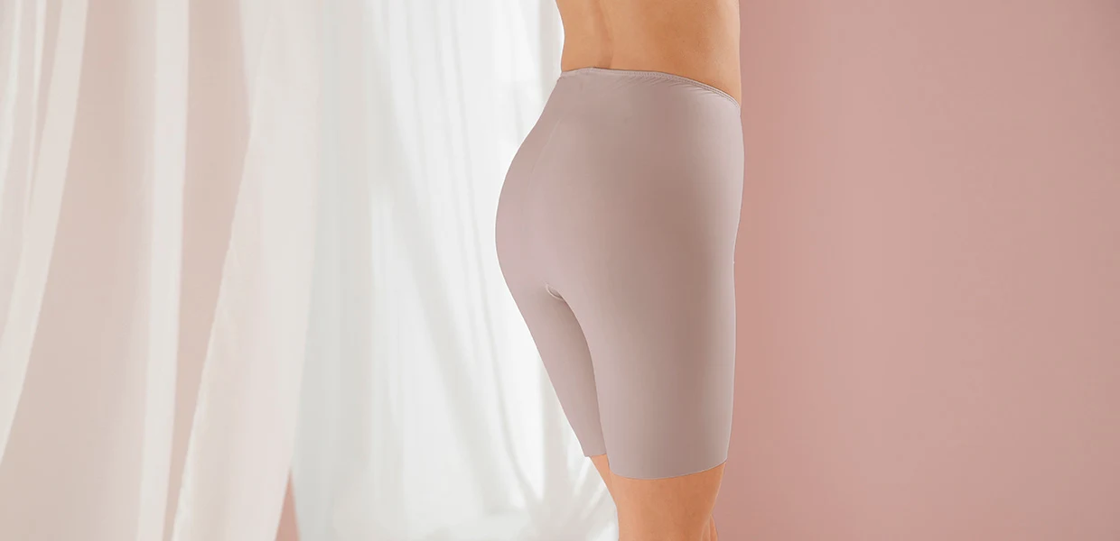 Hautfarbene nahtlose Unterwäsche-Shorts aus elastischem Material, seitlich und von hinten fotografiert, vor einem rosa Hintergrund mit weißen Vorhängen.