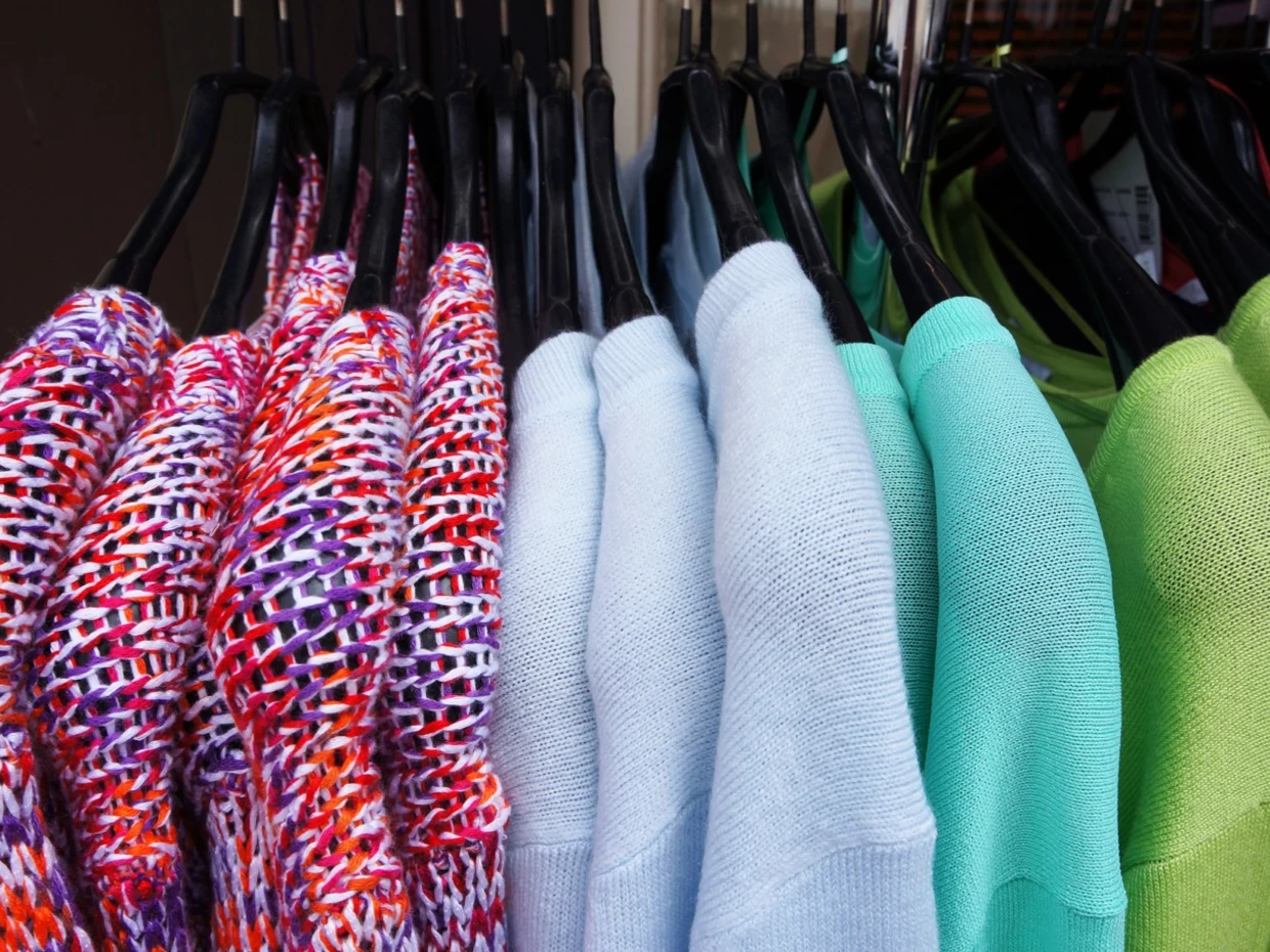 Bunte Pullover aus Strickstoff und einfarbige Pullover in Pastellfarben auf schwarzen Kleiderbügeln. Bunte Pullover aus Strickstoff und einfarbige Pullover in Pastellfarben auf schwarzen Kleiderbügeln.