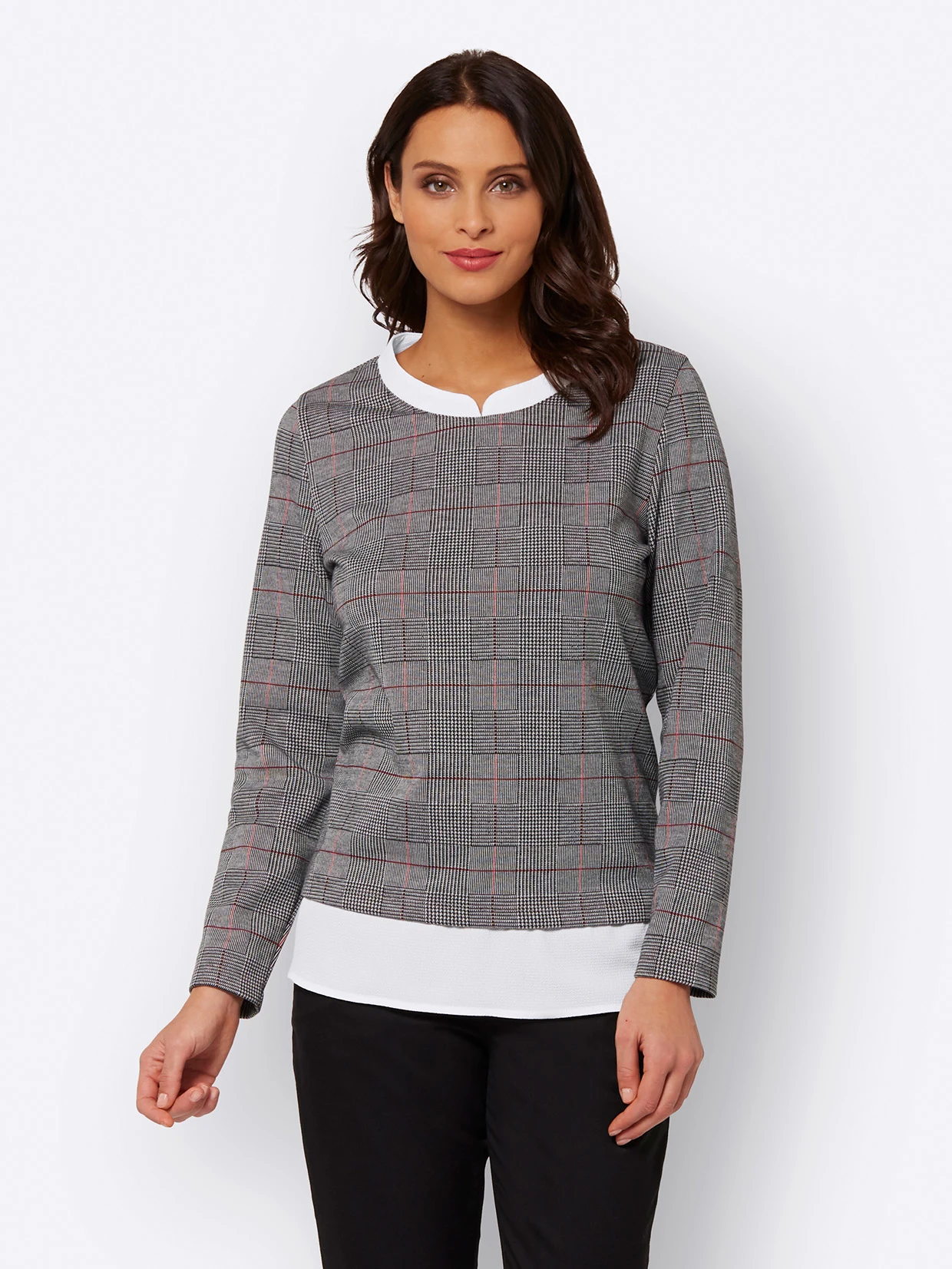 Das weibliche Model trägt einen Langarm-Pullover mit grau-weißem Karomuster, roten Akzenten und weißem Einsatz am Saum, kombiniert mit schwarzer Hose.