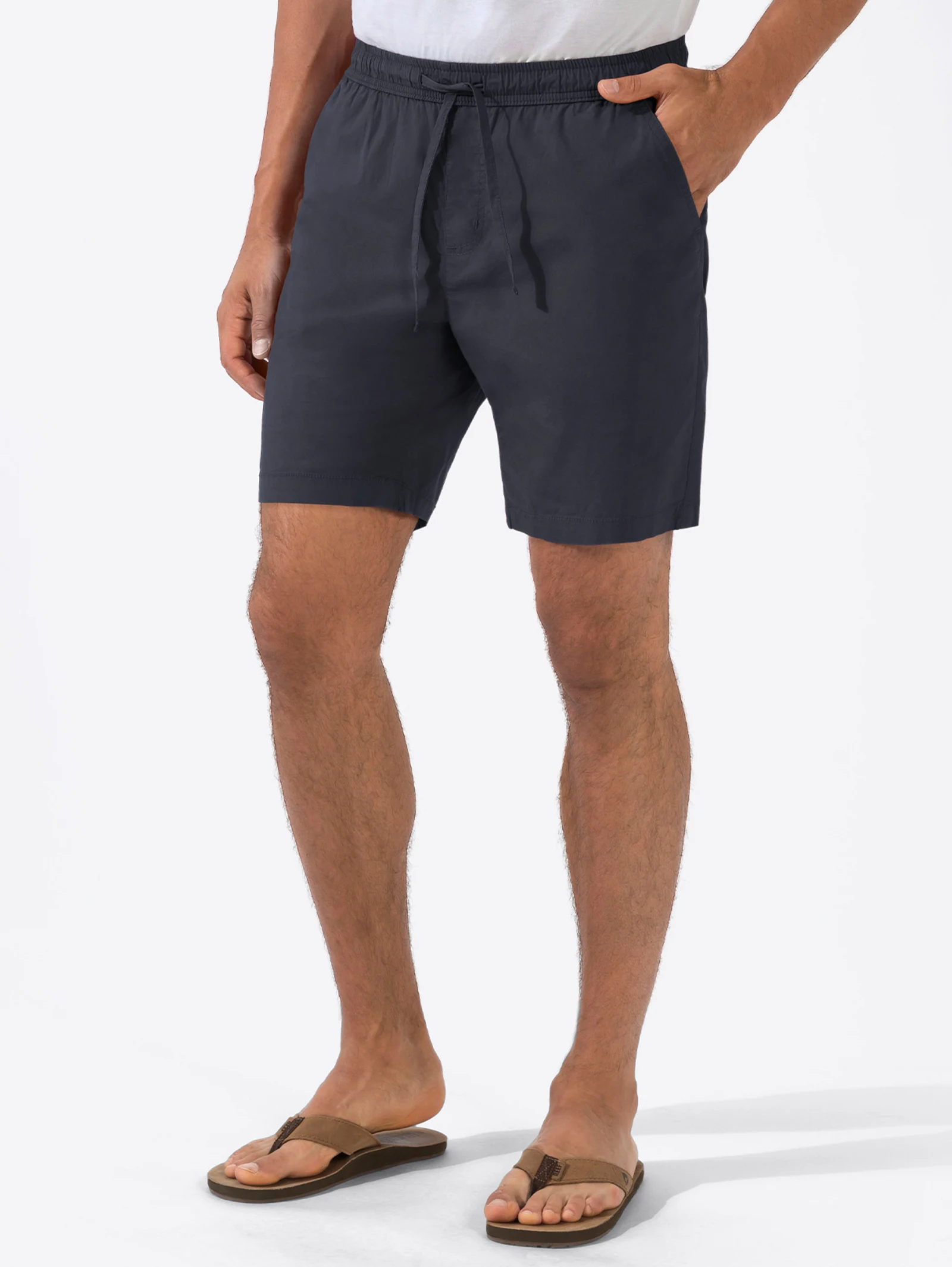 Dunkelblaue Shorts mit Kordelzug, getragen von einem Mann, kombiniert mit braunen Flip-Flops und weißem Oberteil vor weißem Hintergrund. Dunkelblaue Shorts mit Kordelzug, getragen von einem Mann, kombiniert mit braunen Flip-Flops und weißem Oberteil vor weißem Hintergrund.