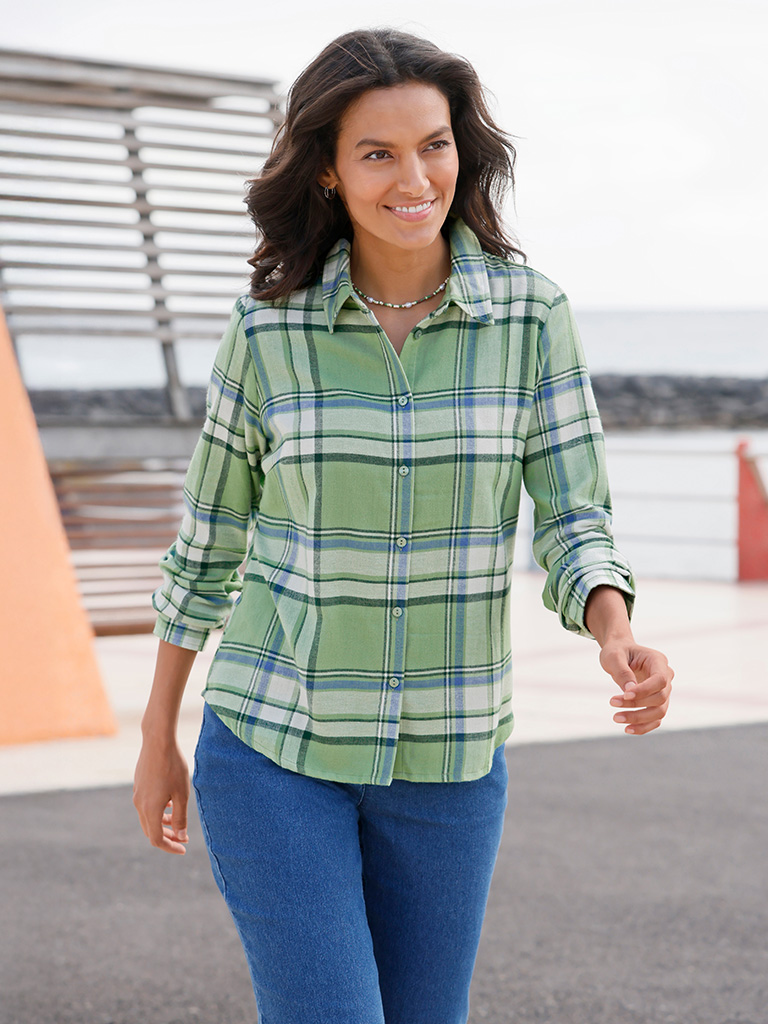 Ein Model trägt eine eucalyptusfarbene Karobluse mit hochgekrempelten Ärmeln und blaue Jeans, stehend im Freien.