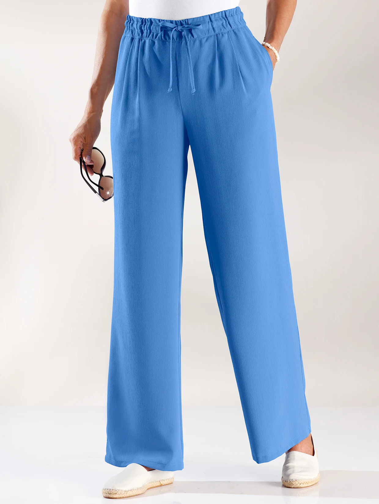 Weite, blaue Damenhose mit elastischem Bund und Kordelzug, kombiniert mit weißen Espadrilles. Weite, blaue Damenhose mit elastischem Bund und Kordelzug, kombiniert mit weißen Espadrilles.