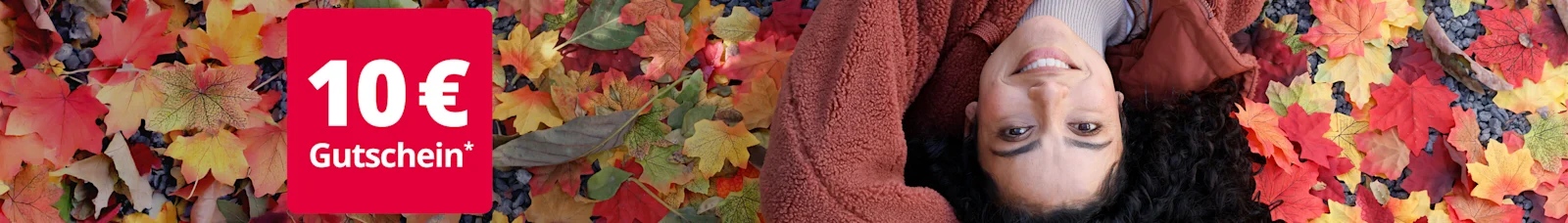 Eine junge, lächelnde Frau liegt auf dem Rücken in buntem Herbstlaub. Sie trägt eine kuschelige, rostbraune Fleece-Jacke. Links oben im Bild ist ein rotes Feld mit der Aufschrift '10 € Gutschein*' zu sehen.