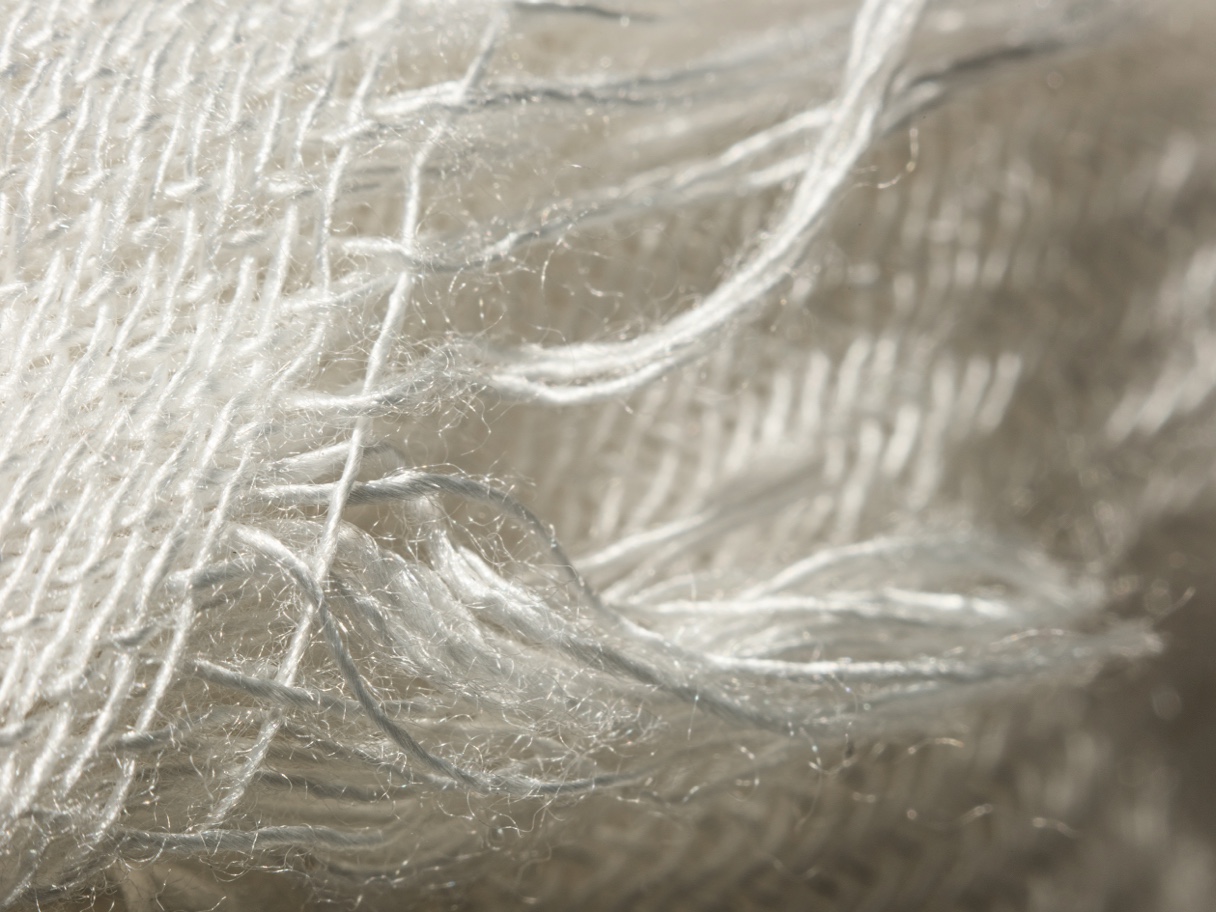 Close-up van witte geweven stof met losse vezels en een textuur van draden.