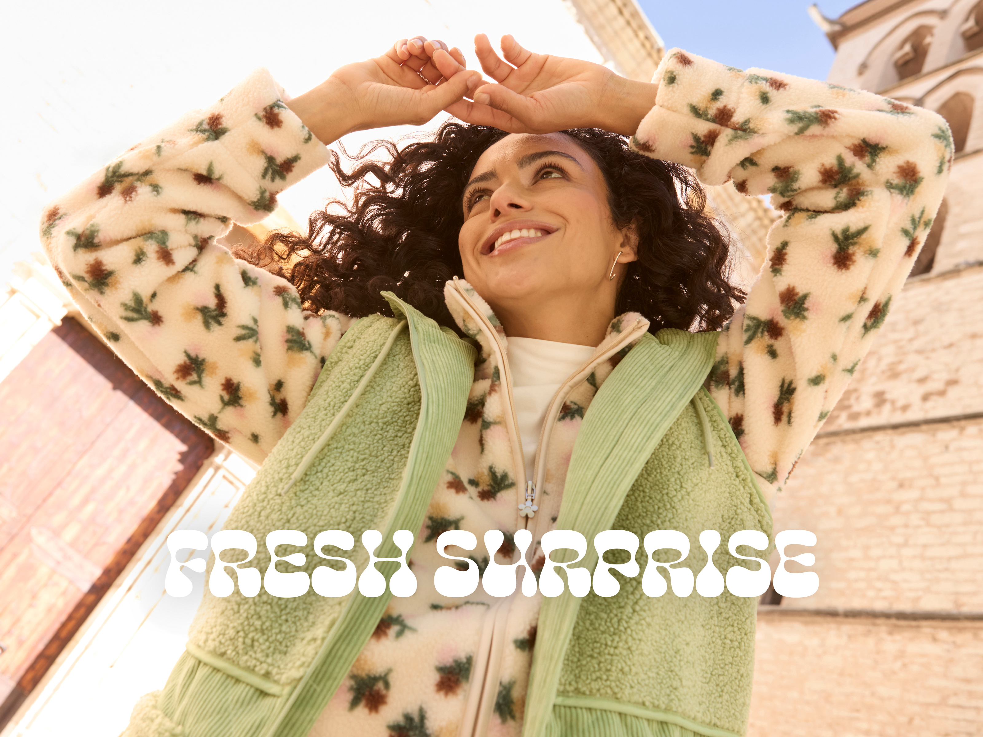 Werbebanner mit Model in Fleecejacke mit Blümchen-Dessin und hellgrüner Fleeceweste mit Text: Fresh Surprise in Schmuckschrift
