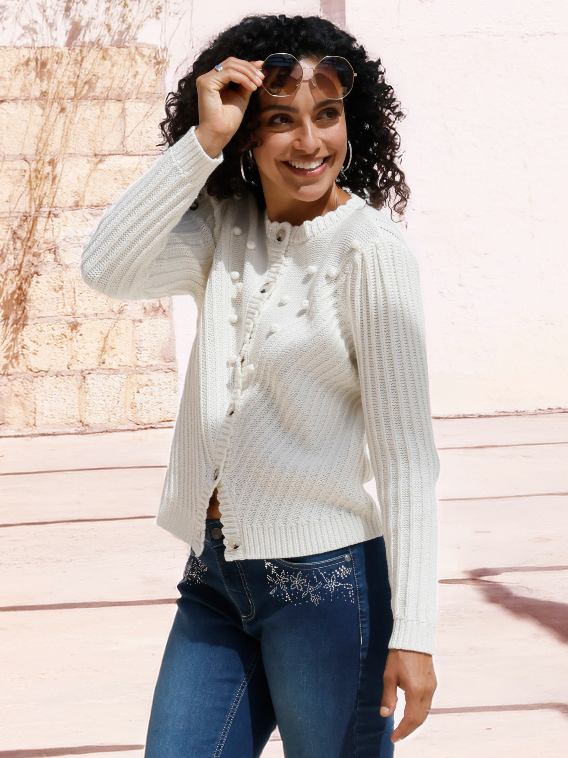 Model in weißer Strickjacke im Landhausstil über Jeans mit Glitzersternchen
