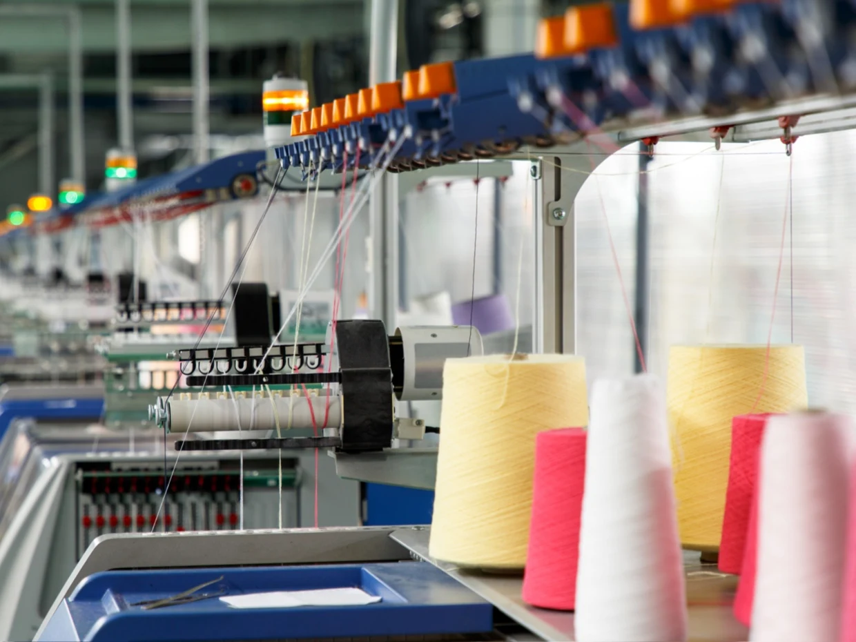 Textilmaschinen in einer Fabrik produzieren Garn, im Vordergrund sind gelbe, weiße und rote Garnspulen zu sehen. Textilmaschinen in einer Fabrik produzieren Garn, im Vordergrund sind gelbe, weiße und rote Garnspulen zu sehen.