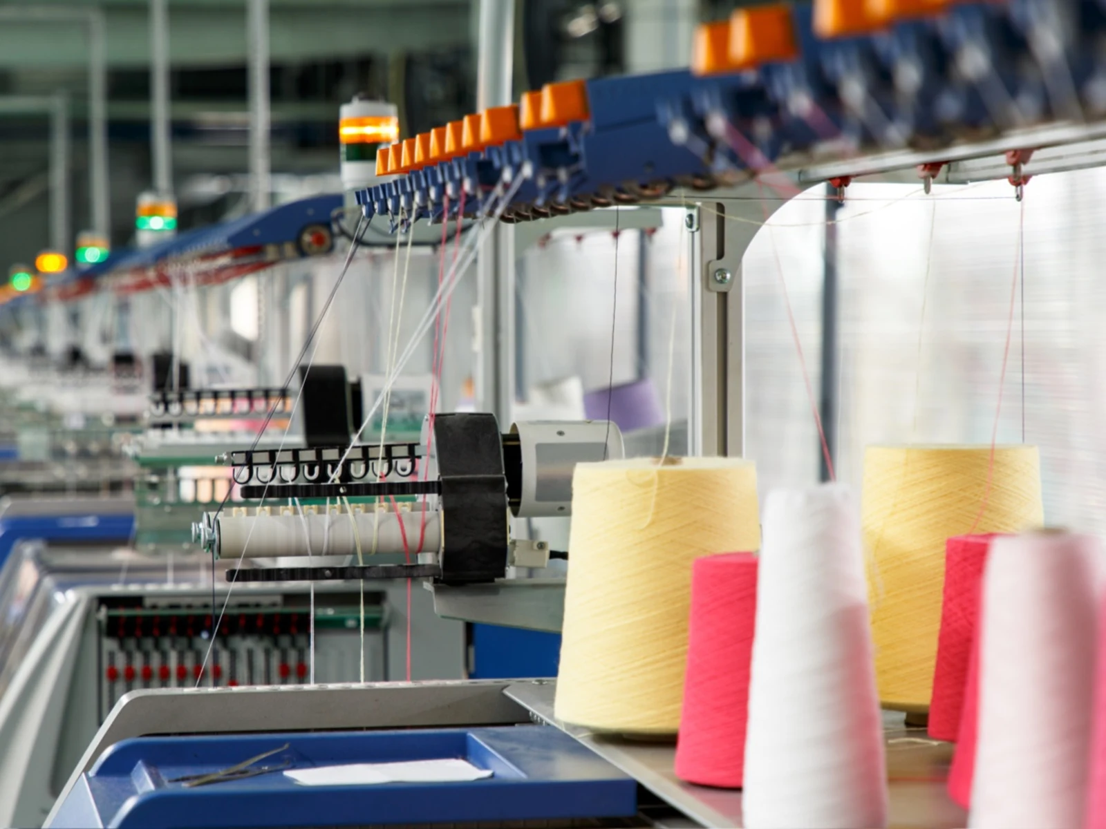 Textilmaschinen in einer Fabrik produzieren Garn, im Vordergrund sind gelbe, weiße und rote Garnspulen zu sehen. Textilmaschinen in einer Fabrik produzieren Garn, im Vordergrund sind gelbe, weiße und rote Garnspulen zu sehen.