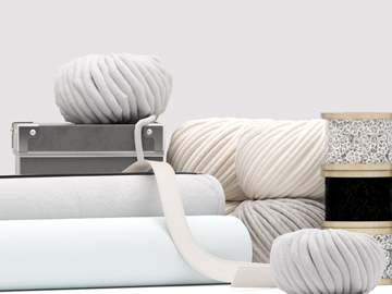 Wollknäuel in Grautönen, Stoffrollen und Spitzenbänder vor neutralem Hintergrund.