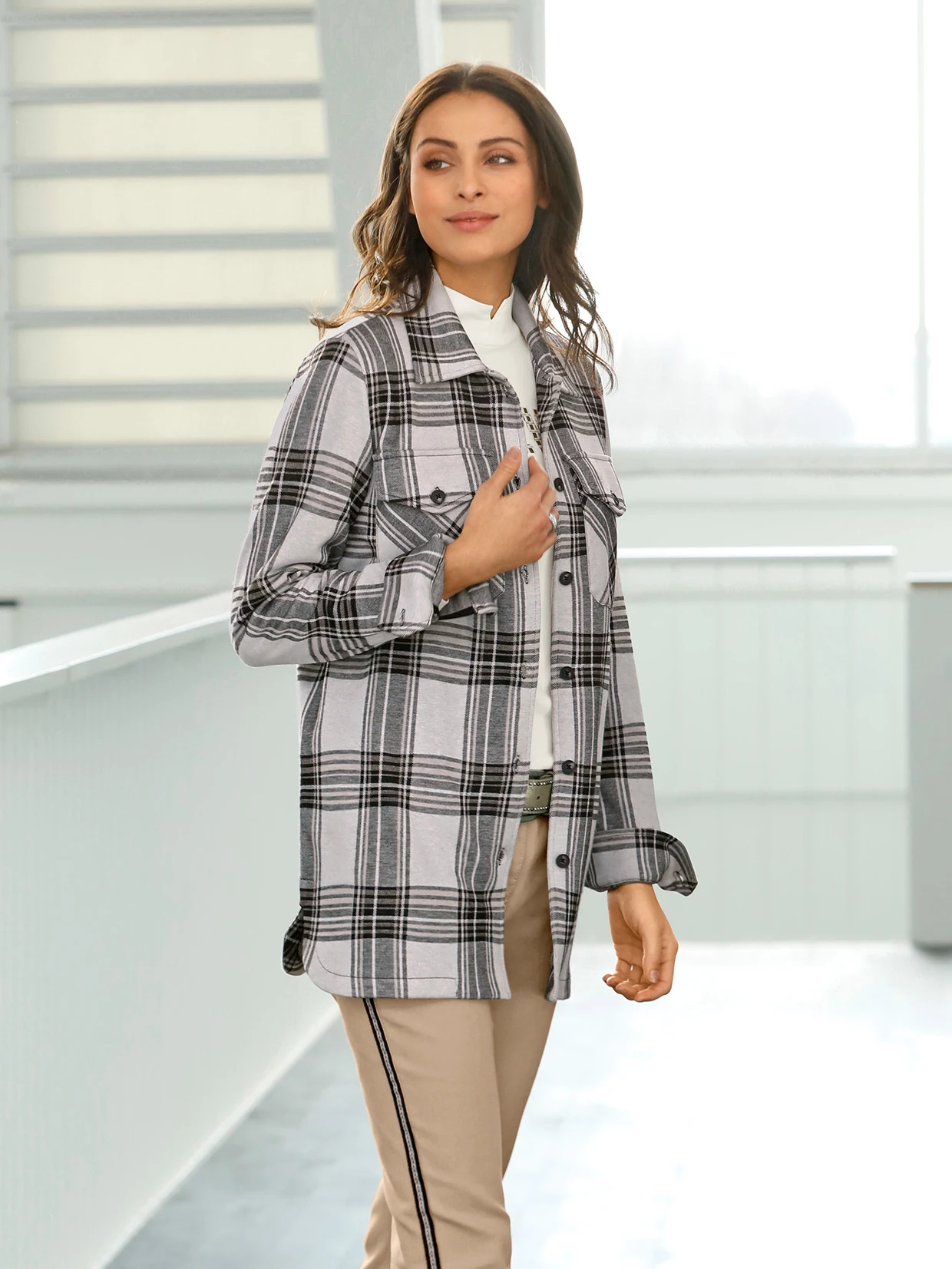 Frau trägt ein kariertes Hemd in Grau und Schwarz über einem weißen Oberteil kombiniert mit beigefarbenen Hosen mit schwarzem Streifen.
