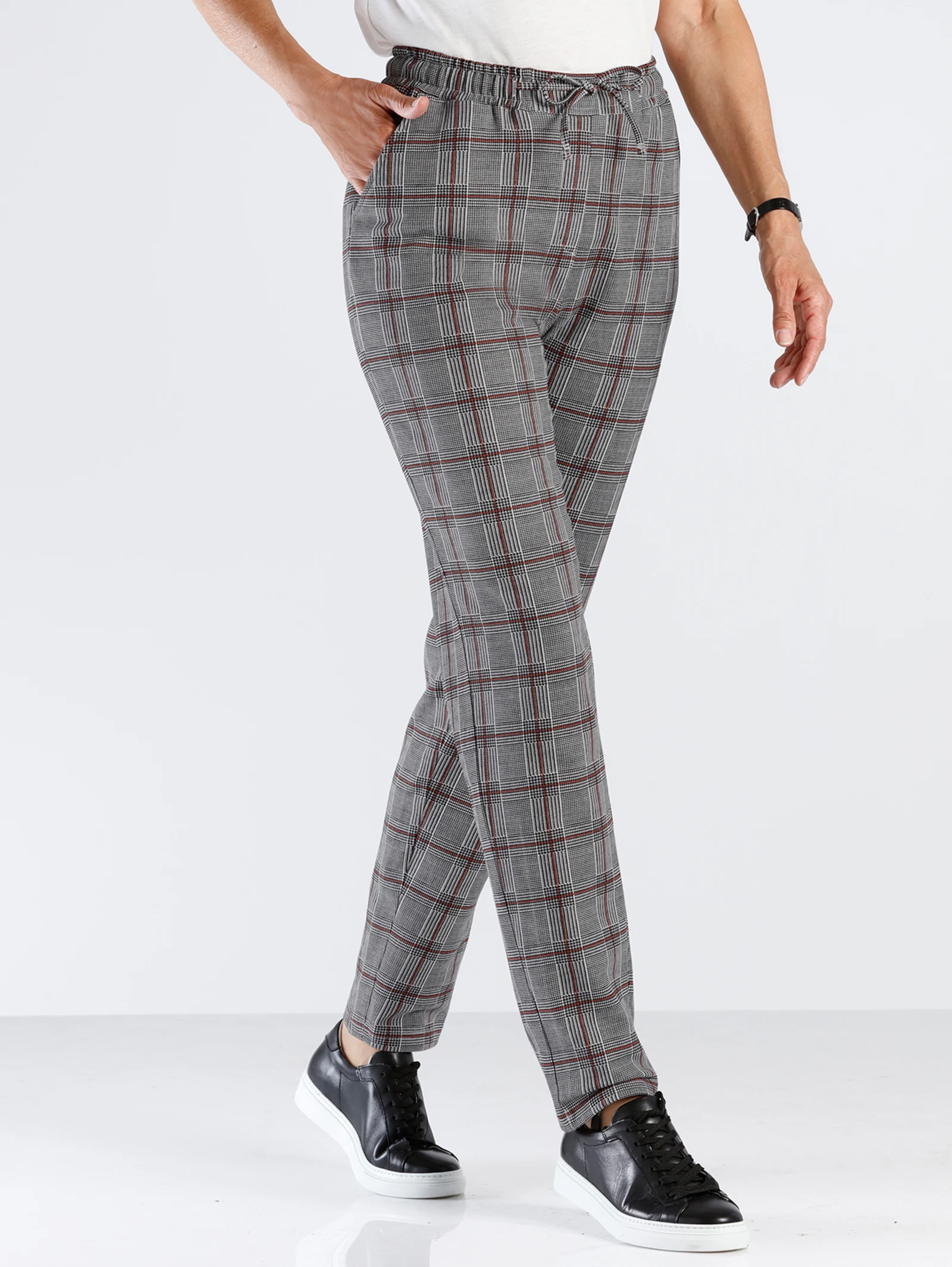 Graue karierte Damenhose mit elastischem Bund, kombiniert mit schwarzen Sneakern und weißem Oberteil. Graue karierte Damenhose mit elastischem Bund, kombiniert mit schwarzen Sneakern und weißem Oberteil.