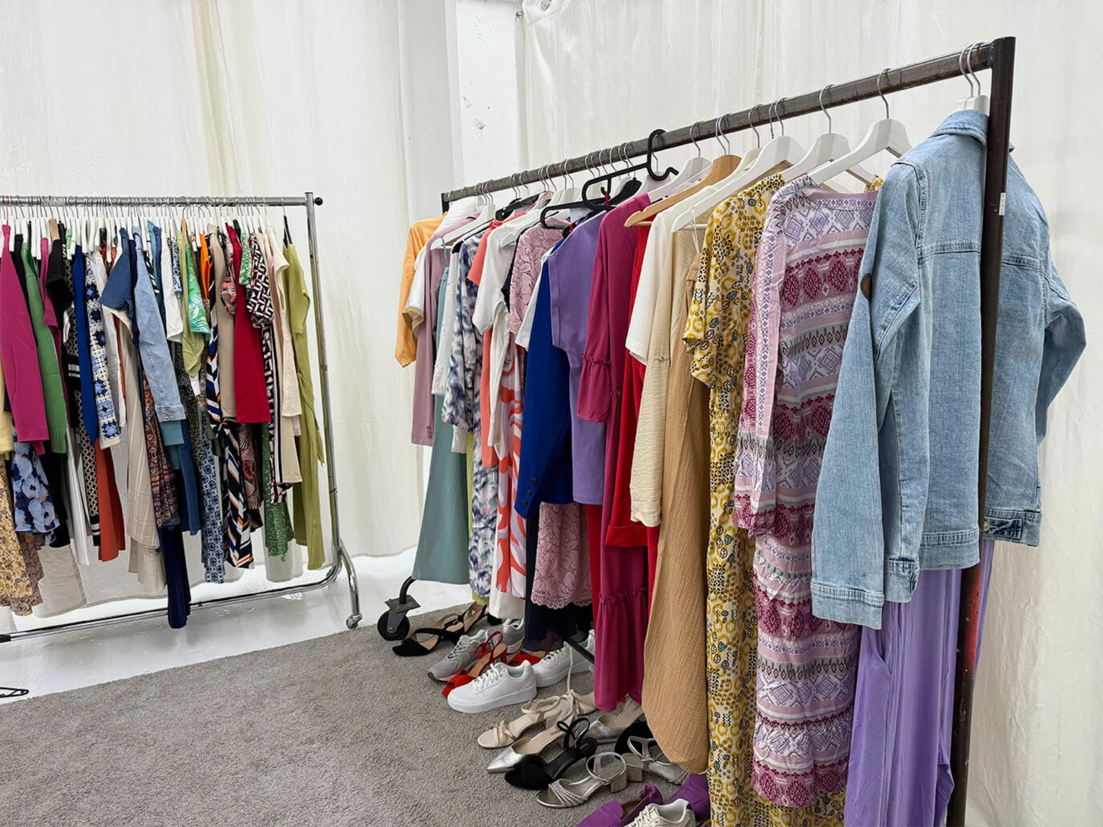Zwei Kleiderstangen mit verschiedenen Kleidungsstücken in verschiedenen Farben und Stilen sowie Schuhen in einem hellen Raum. Zwei Kleiderstangen mit verschiedenen Kleidungsstücken in verschiedenen Farben und Stilen sowie Schuhen in einem hellen Raum.