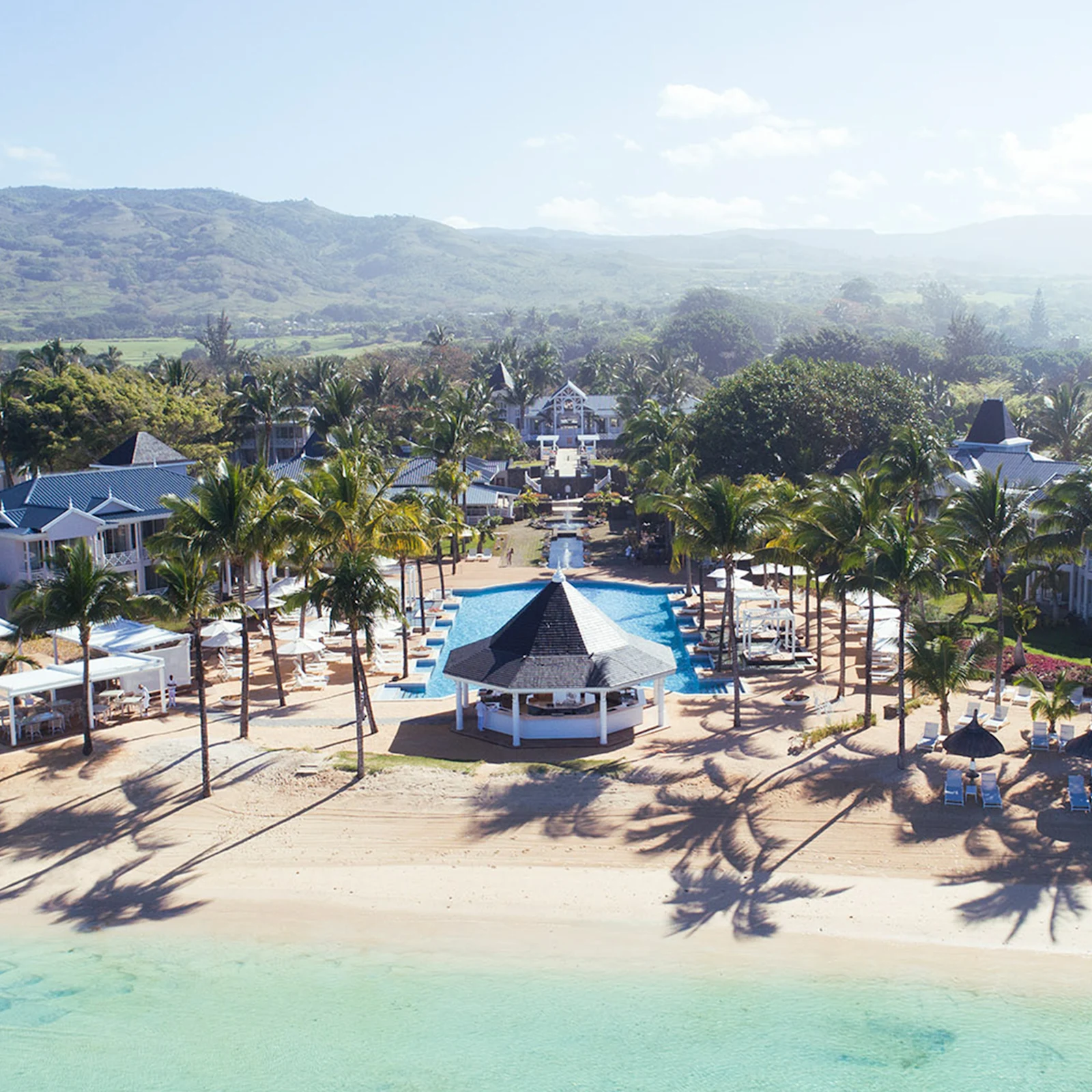 Luftaufnahme eines Strandhotels mit Palmen, Pool, Pavillon und Bergen im Hintergrund. Heller Sandstrand und klares Wasser. Luftaufnahme eines Strandhotels mit Palmen, Pool, Pavillon und Bergen im Hintergrund. Heller Sandstrand und klares Wasser.