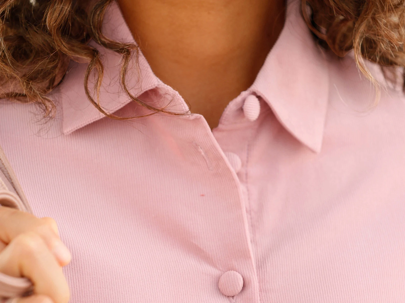 Ein Model trägt eine rosa Bluse mit umgekrempelten Ärmeln und dunkler Hose.