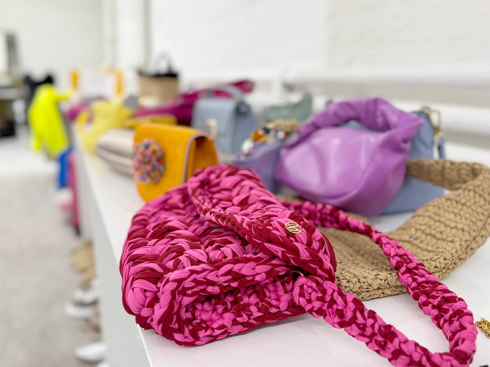 Mehrere Taschen in verschiedenen Farben liegen auf einer weißen Fläche. Eine auffällige pinke Tasche ist im Vordergrund. Der Hintergrund ist unscharf. Mehrere Taschen in verschiedenen Farben liegen auf einer weißen Fläche. Eine auffällige pinke Tasche ist im Vordergrund. Der Hintergrund ist unscharf.