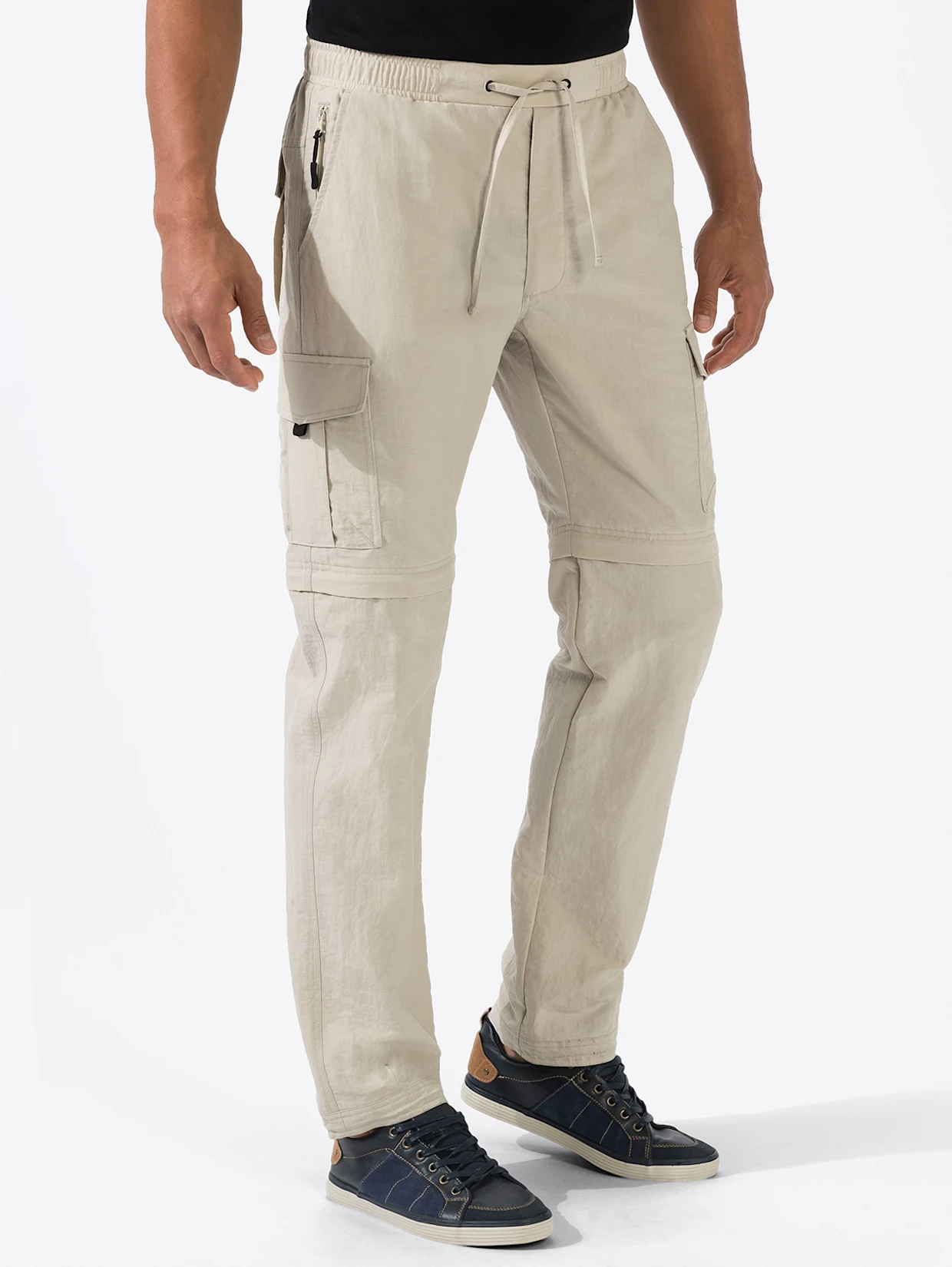 Beige Cargo-Hose mit Taschen, elastischem Bund und Kordelzug, kombiniert mit dunkelblauen Sneakern. Beige Cargo-Hose mit Taschen, elastischem Bund und Kordelzug, kombiniert mit dunkelblauen Sneakern.