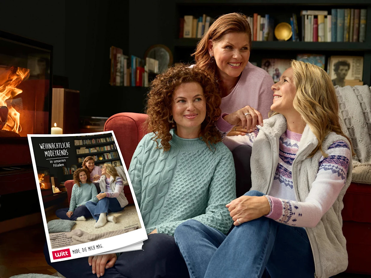 Drei Frauen sitzen gemütlich auf dem Boden vor einem Kamin, tragen warme Pullover und Jeans, im Vordergrund ein Katalog mit dem gleichen Bild.