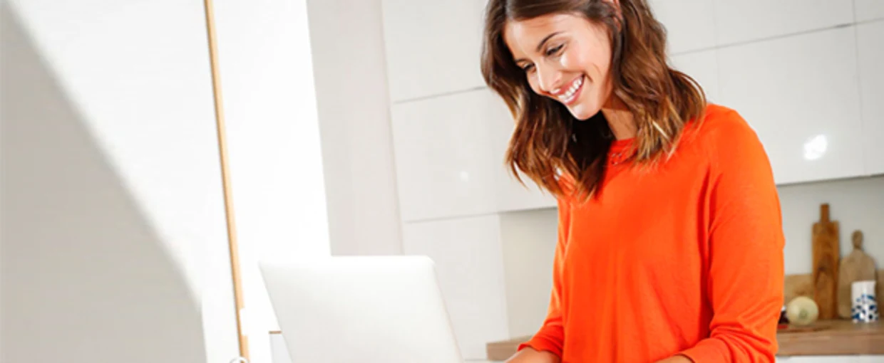 Frau in orangem Pullover arbeitet an einem Laptop in einer modern eingerichteten Küche. Frau in orangem Pullover arbeitet an einem Laptop in einer modern eingerichteten Küche.