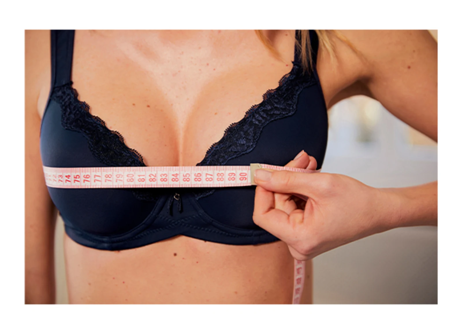 Vrouw meet haar borstomvang met een meetlint terwijl ze een donkerblauwe bh draagt. Vrouw meet haar borstomvang met een meetlint terwijl ze een donkerblauwe bh draagt.