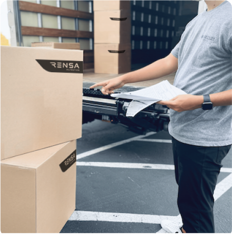 Person checking boxes with a clipboard and paperwork next to a loading truck.