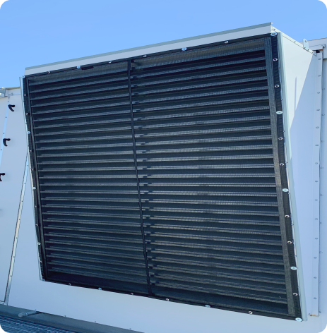 Close-up of a large industrial air conditioning unit's exterior vent on a building rooftop, featuring a black slatted grille.