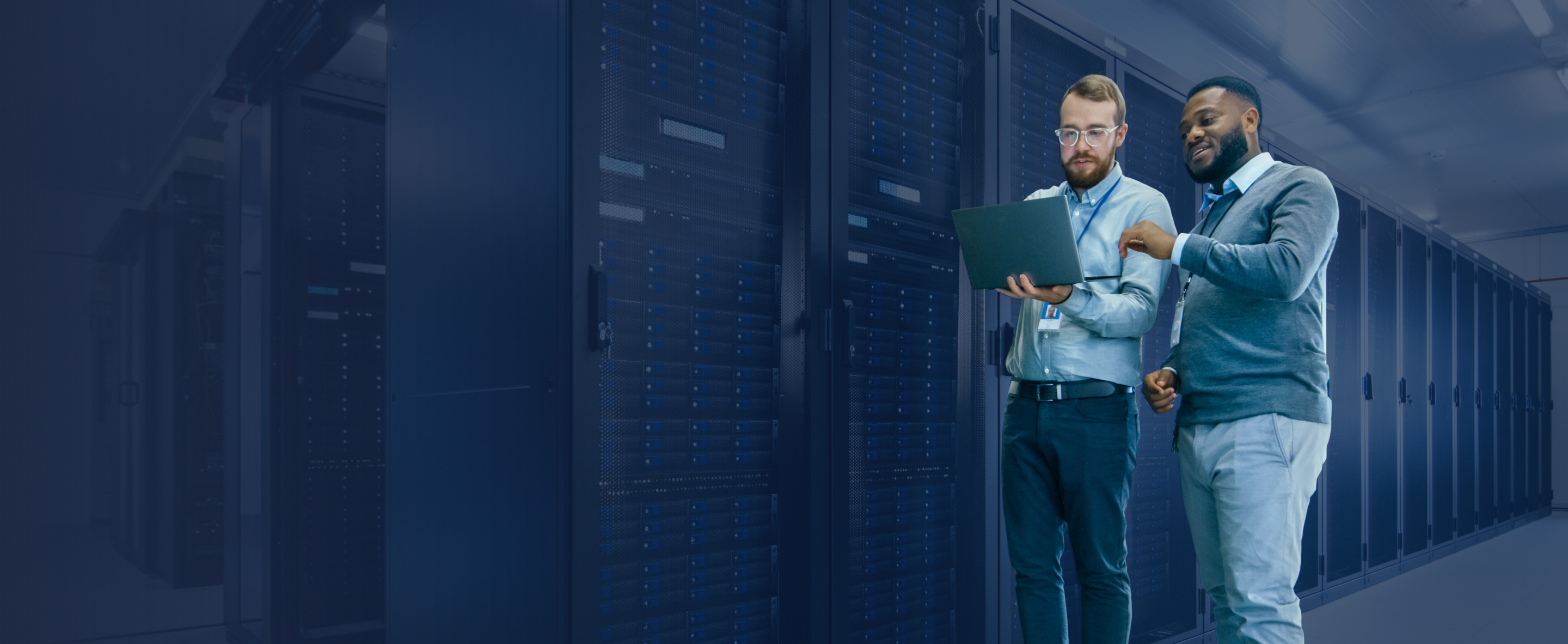 IT professionals in a modern data center analyzing a laptop, surrounded by server racks.