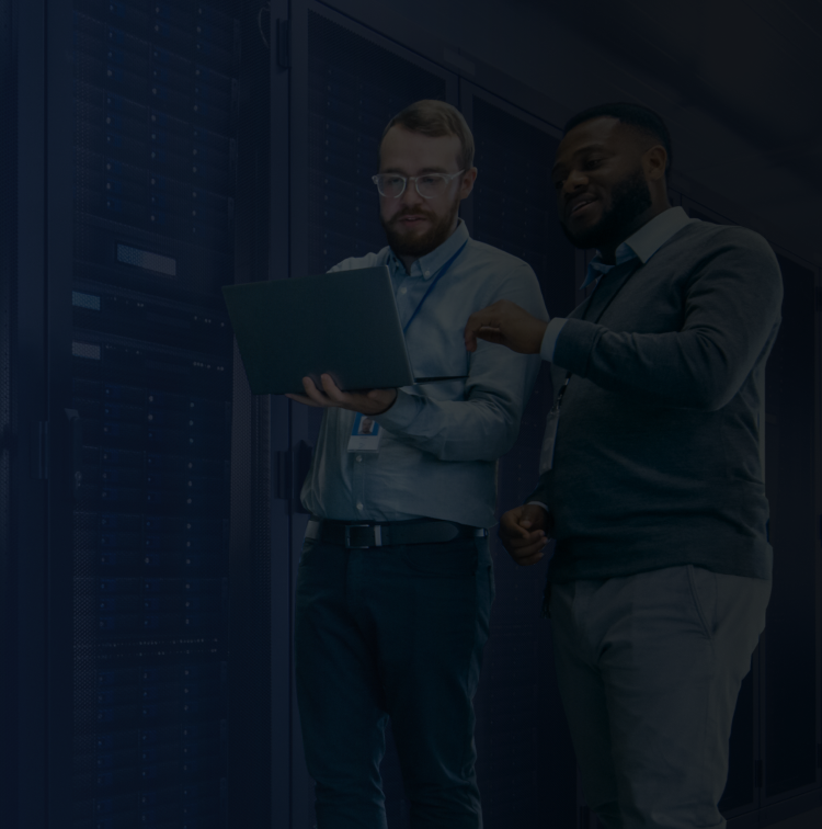 IT professionals in a modern data center analyzing a laptop, surrounded by server racks.