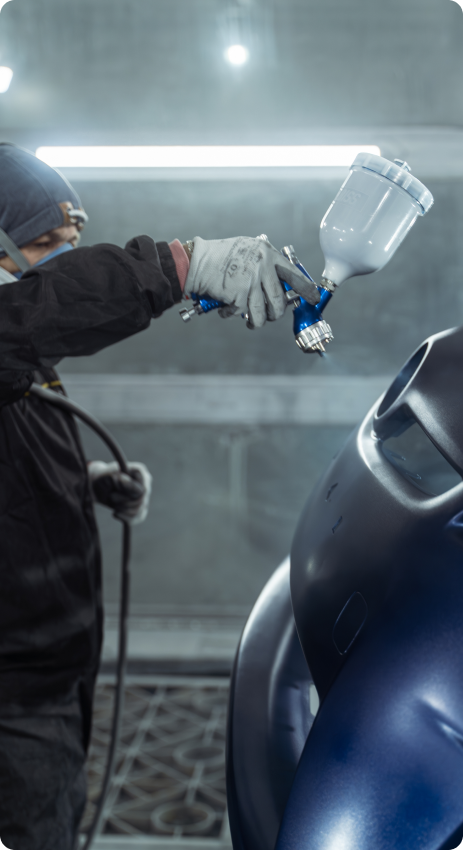 A worker in a mask and gloves is painting a car part with a spray gun.