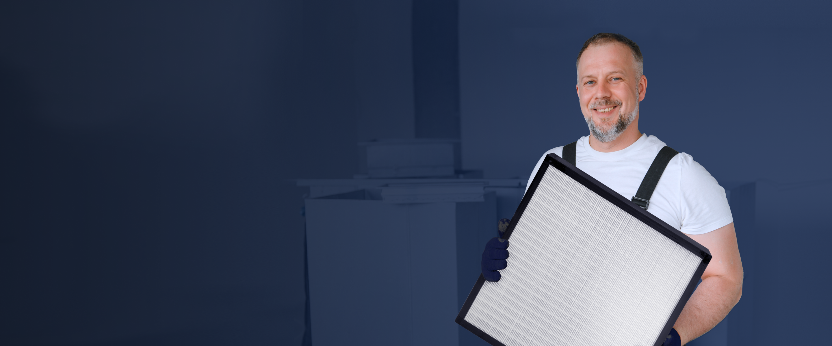 A man wearing a white t-shirt and overalls holds a large rectangular filter against a background.