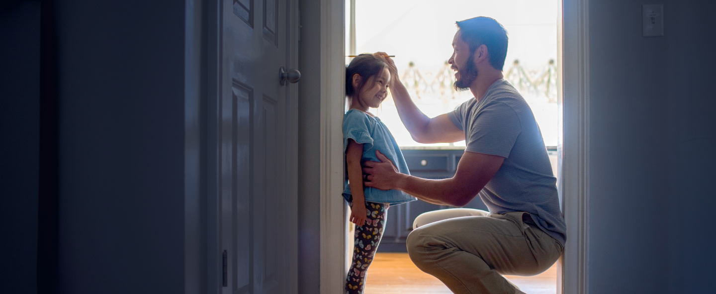 An adult and child with obscured faces look into a brightly lit room from a doorway.