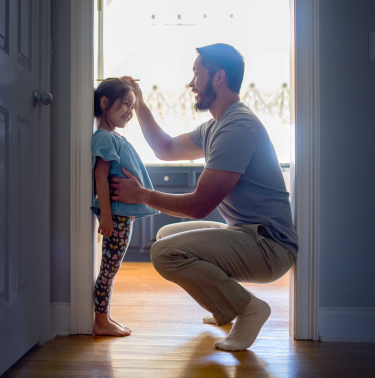 An adult and child with obscured faces look into a brightly lit room from a doorway.