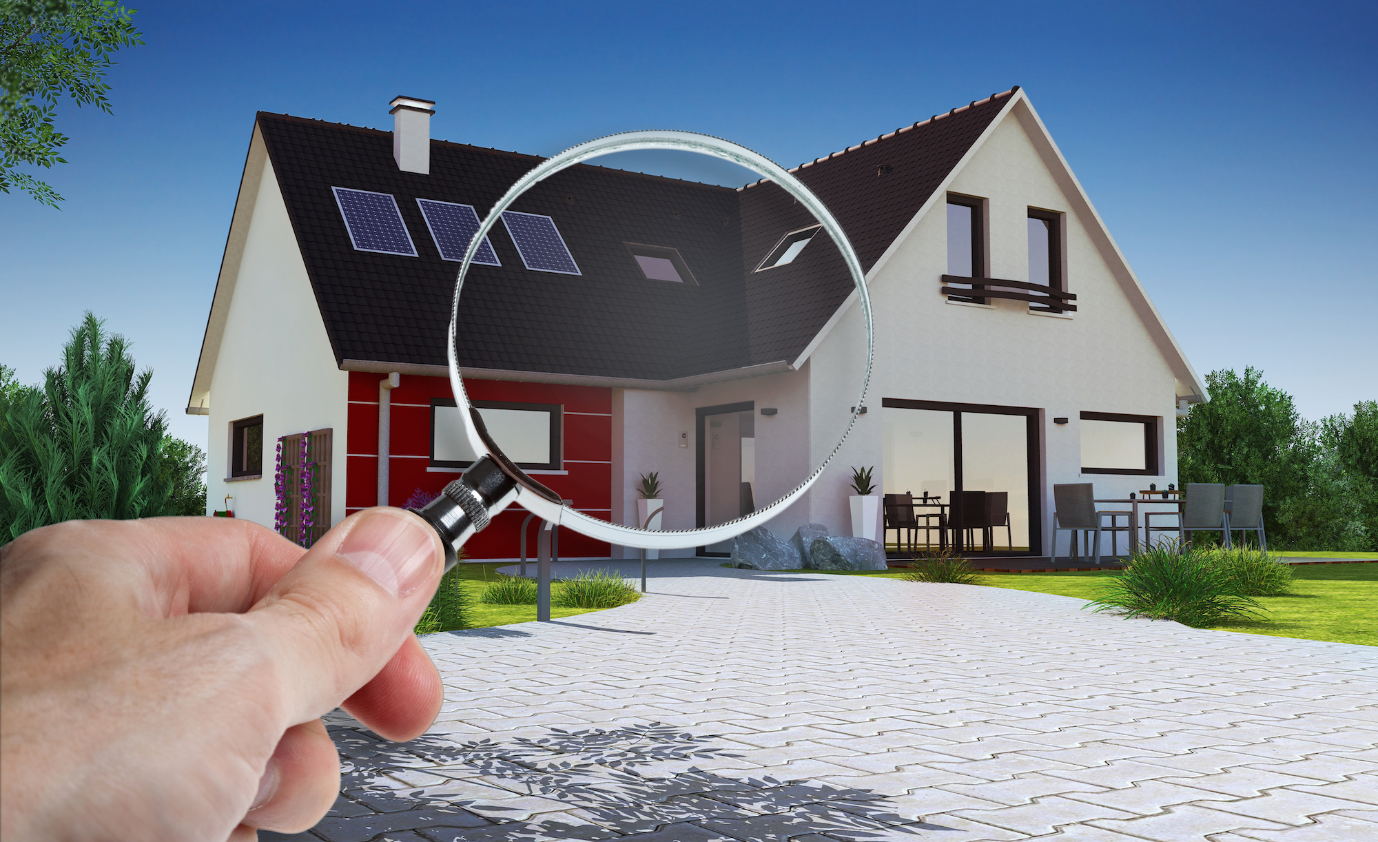 Hand holding a magnifying glass over a house.