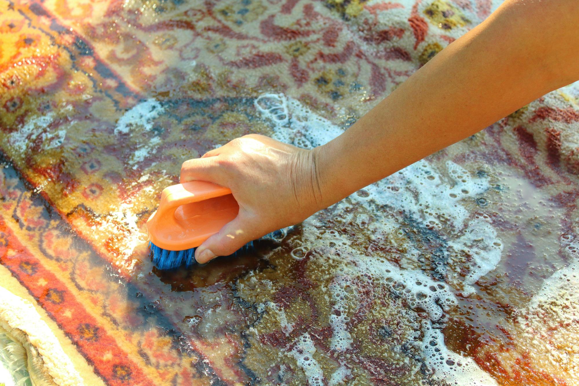 multi colored rug with a hand using a scrubbing sponge 