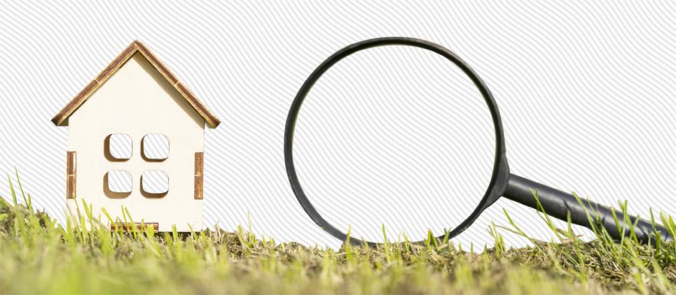 Magnifying glass sits next to miniature house figurine. 