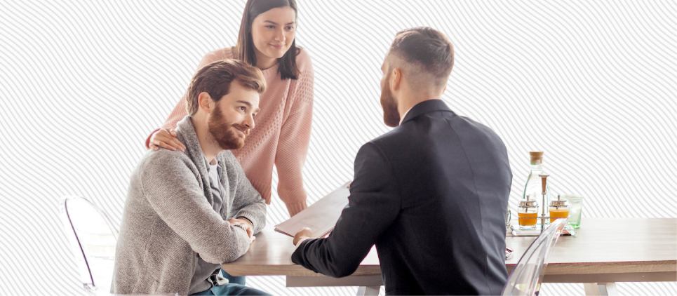 A couple consults with a man holding paperwork at a desk. 