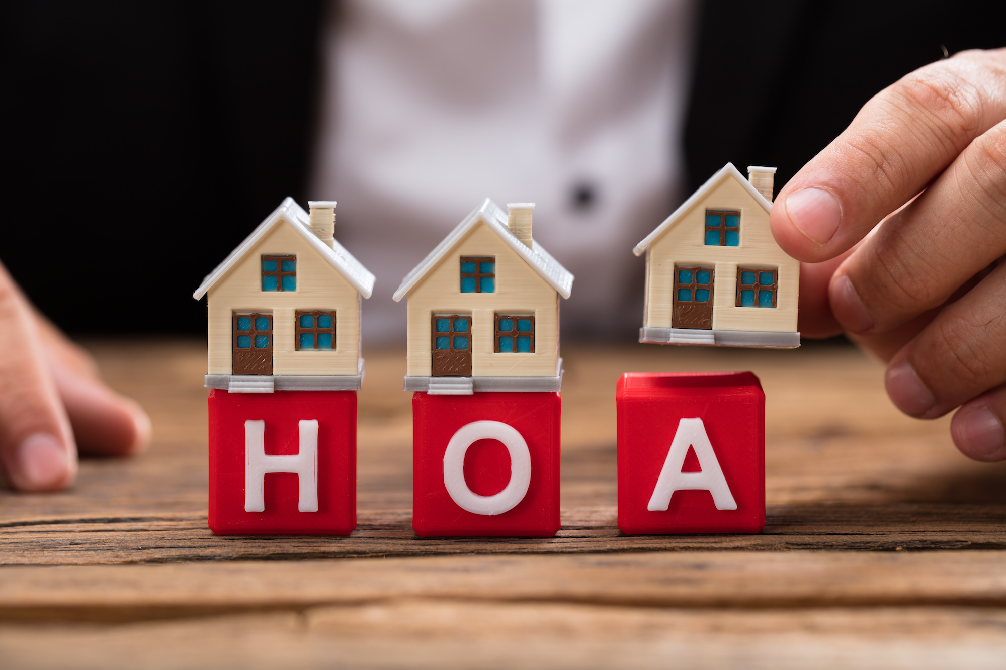 Miniature blocks spelling out "HOA" have small house figurines placed on top of them. 