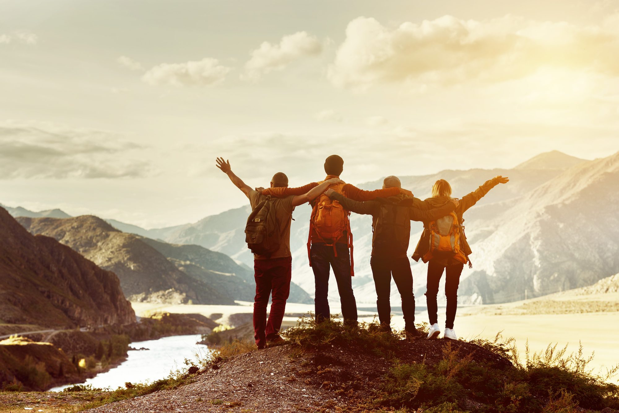 Group of adults with their arms around each other on top of a mountain at sunset.