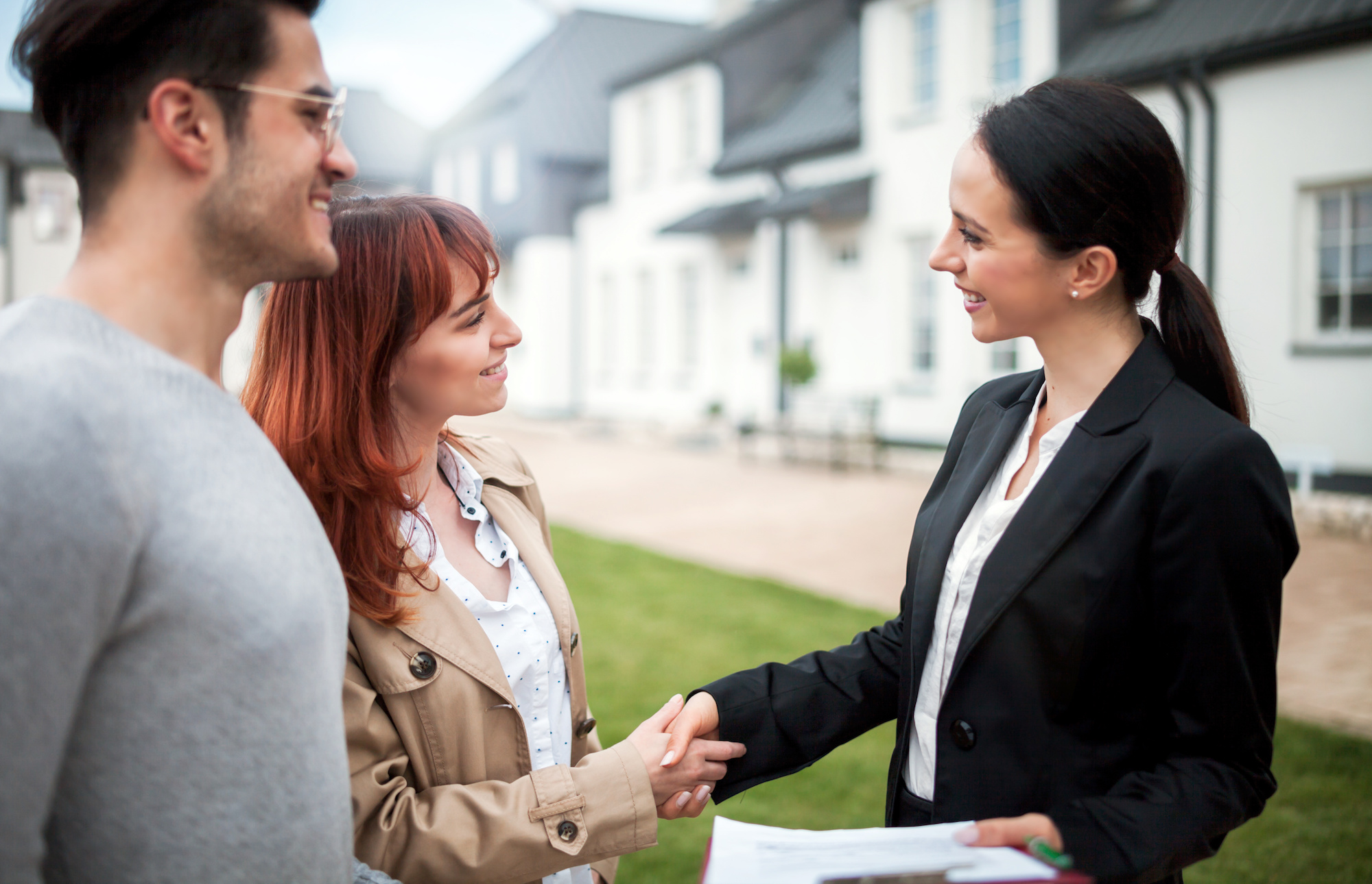 Real estate agent shakes hands with a couple in front of a home. 