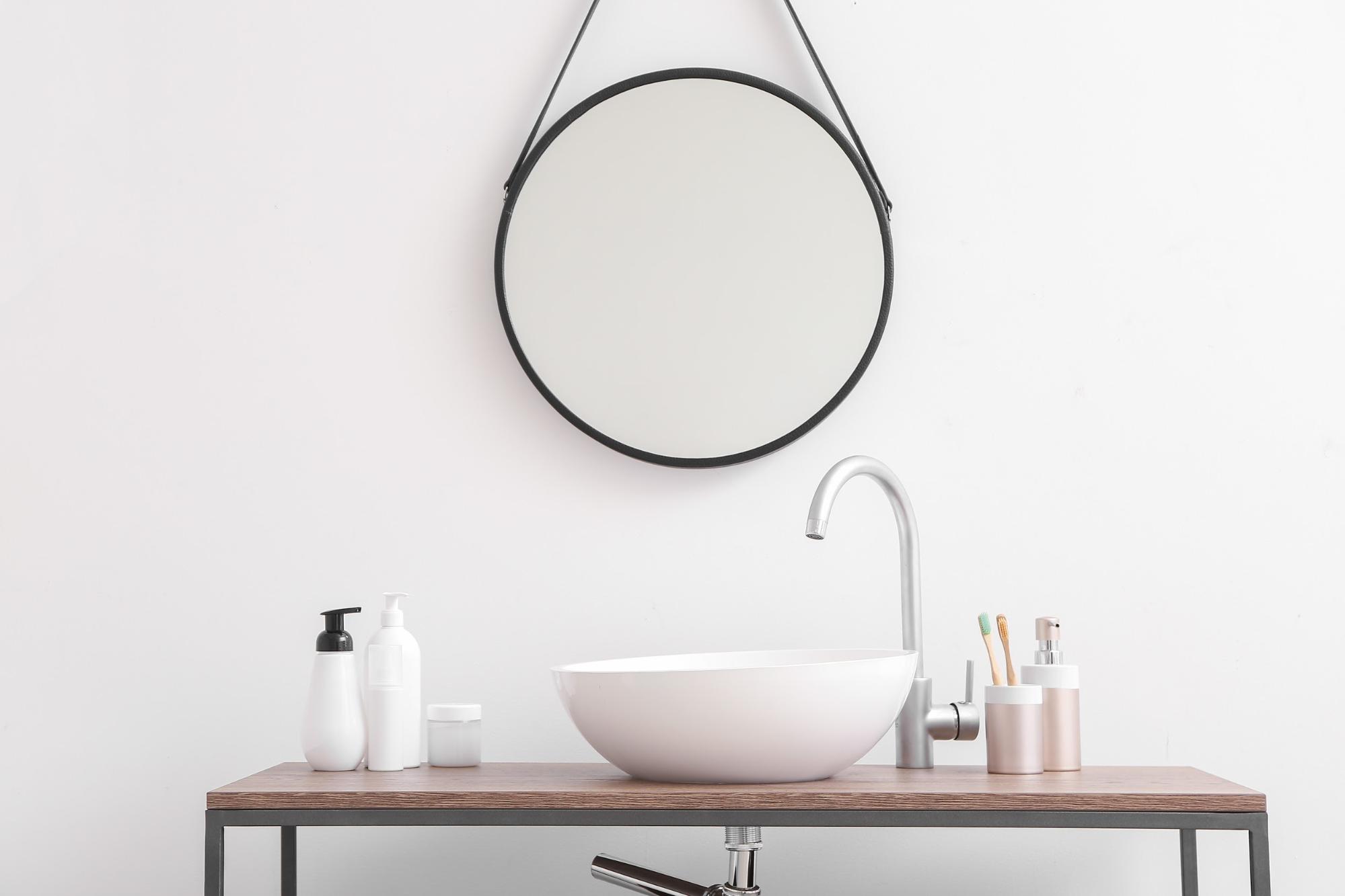 kitchen sink against a white wall with a round mirror 