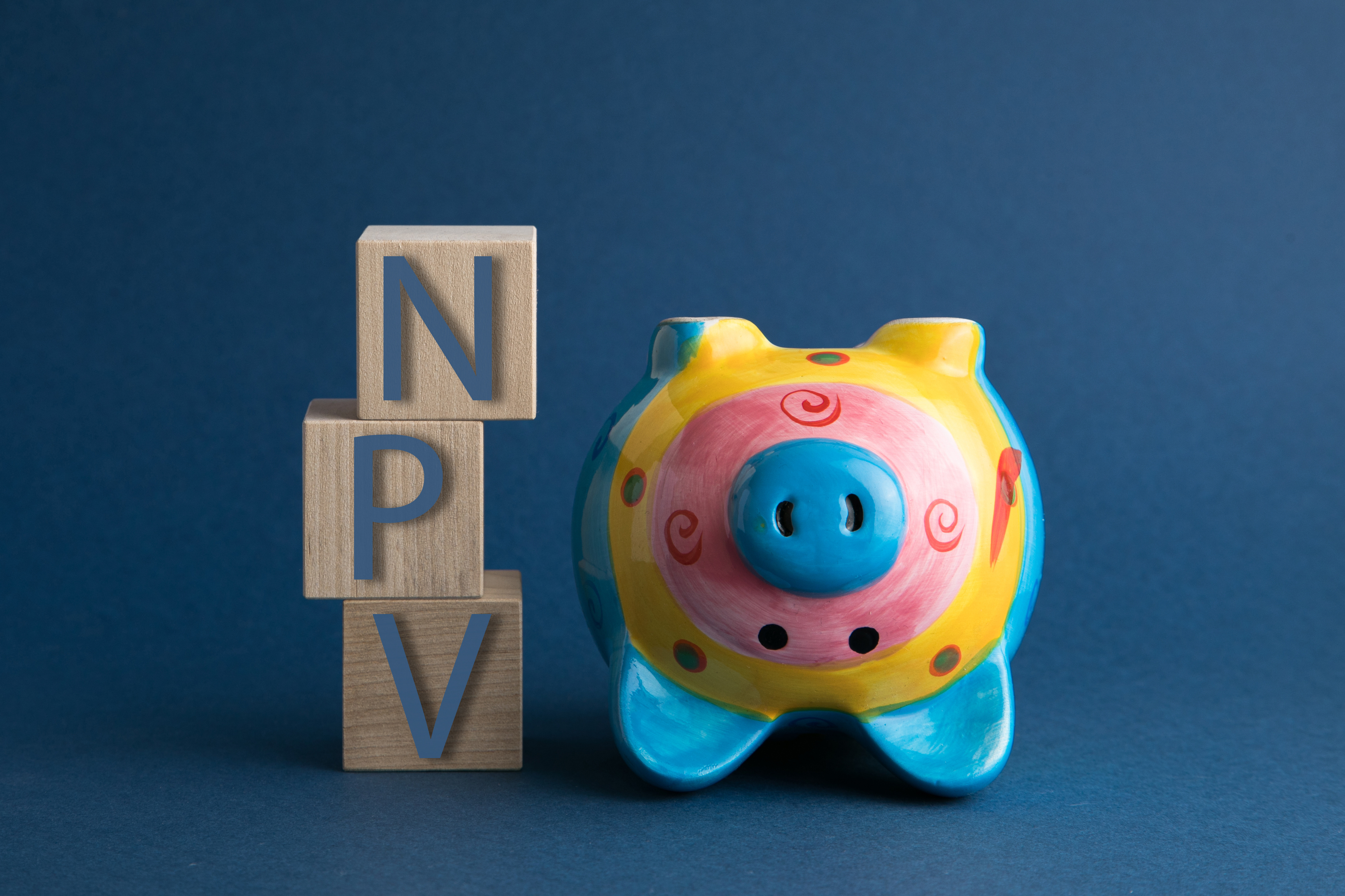 Colorful upside down piggy bank next to 3 blocks stacked with the letters N, P, V. 
