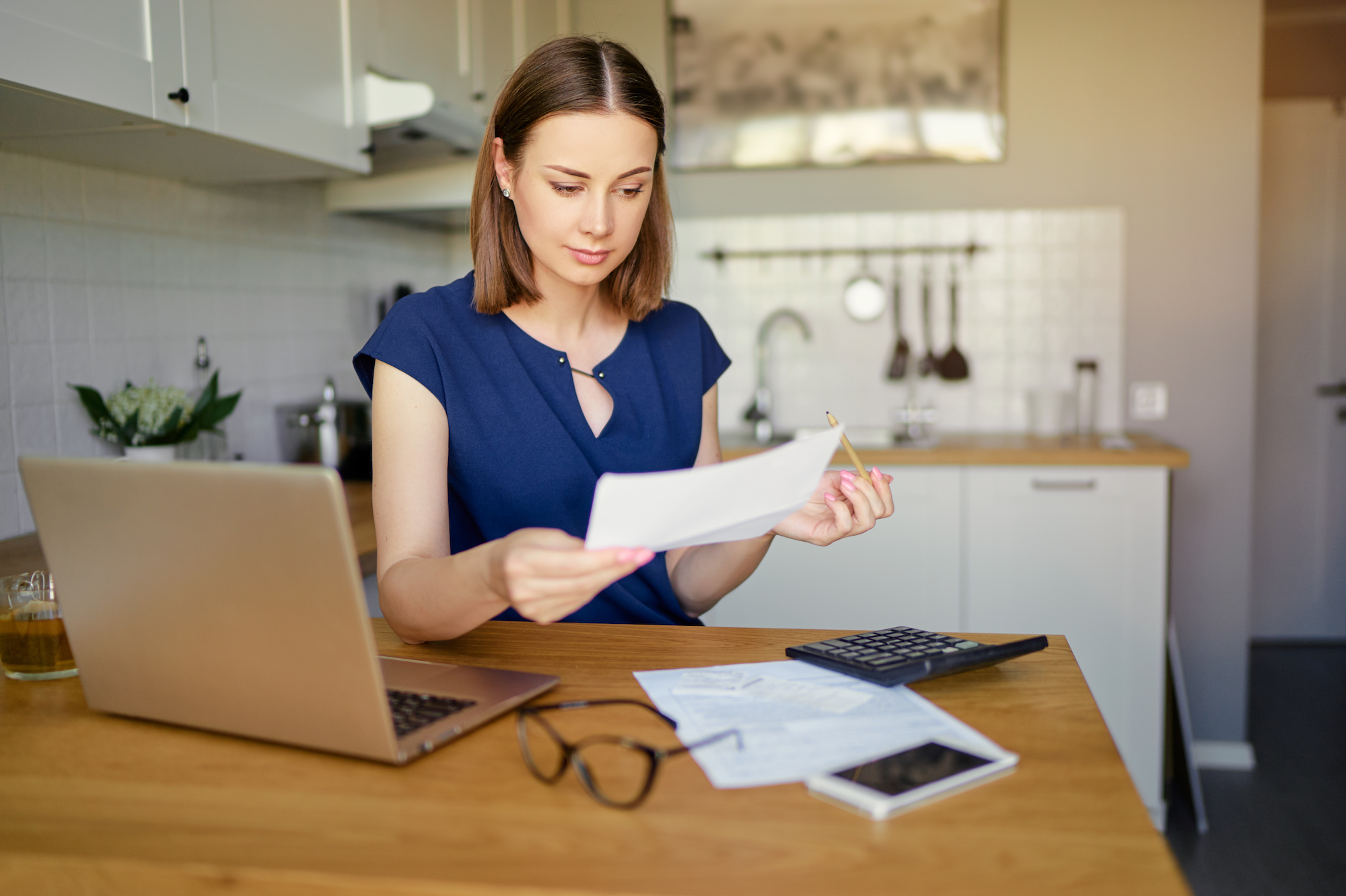 A woman looks over bills in her kitchen in front of a computer.