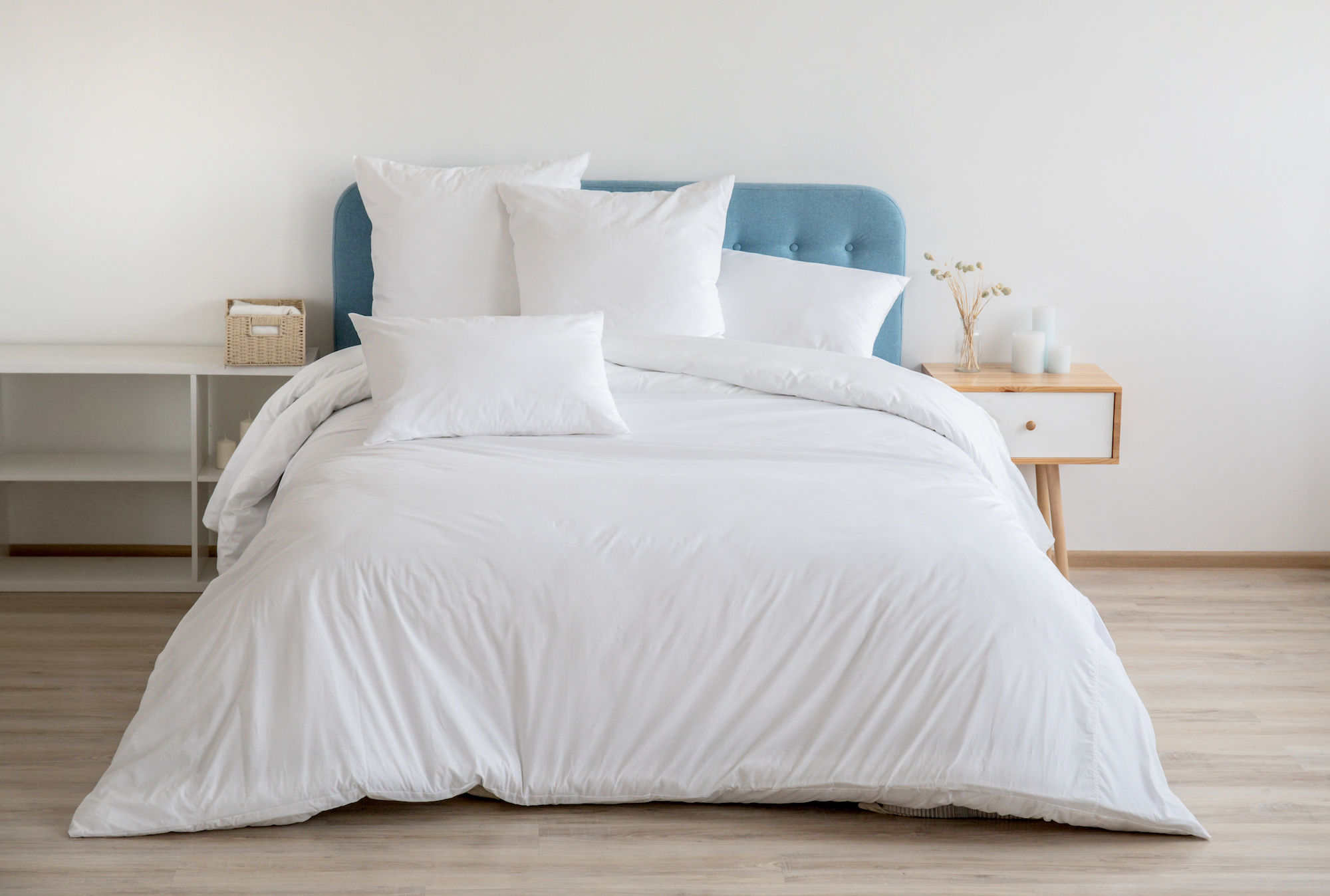 Bed with blue headboard and white duvet cover with matching pillows.