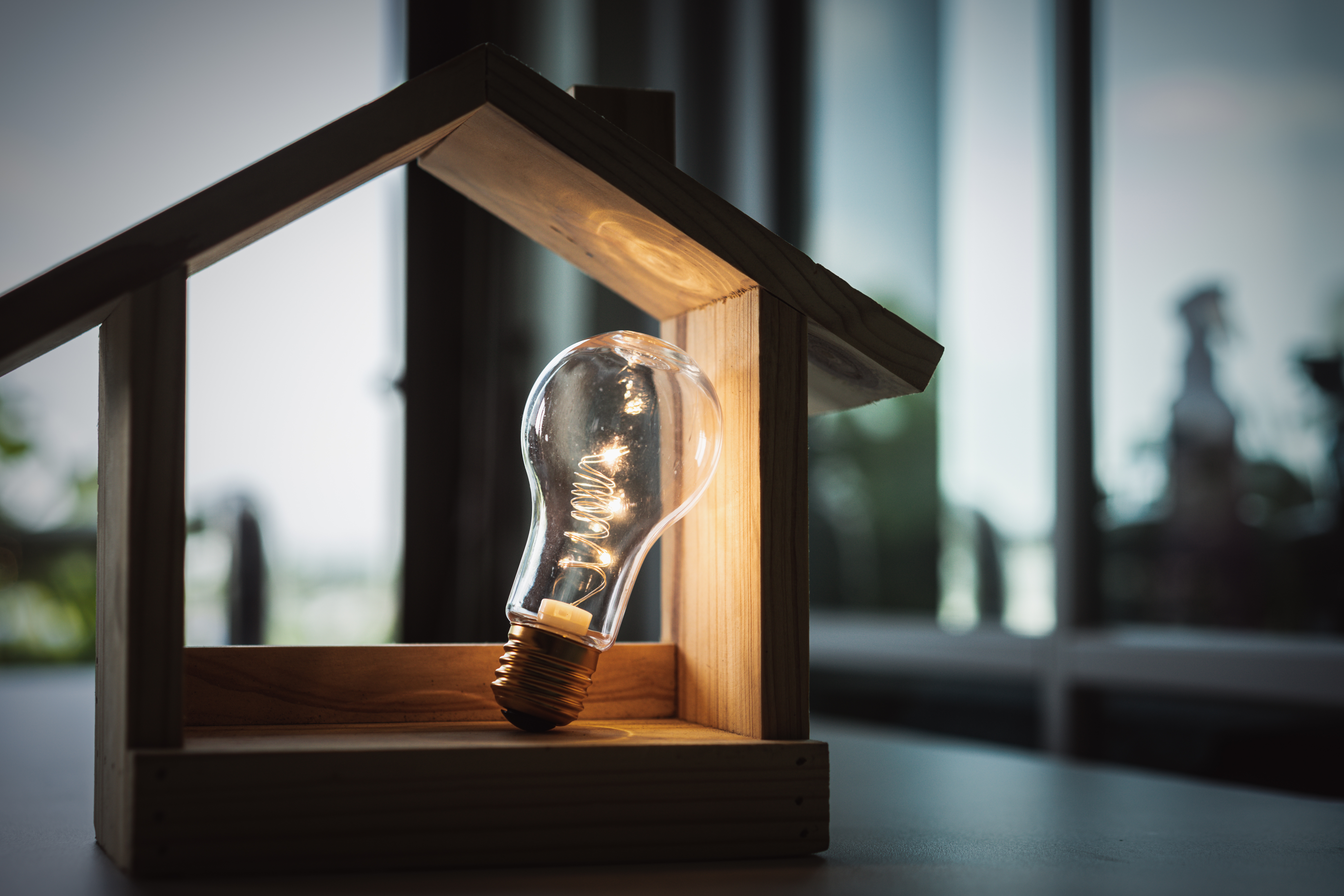 A singular filament lightbulb lights up a miniature wooden house.