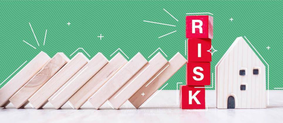 Small wooden planks lean up against stacked block letters that read "risk"next to a miniature wooden house.