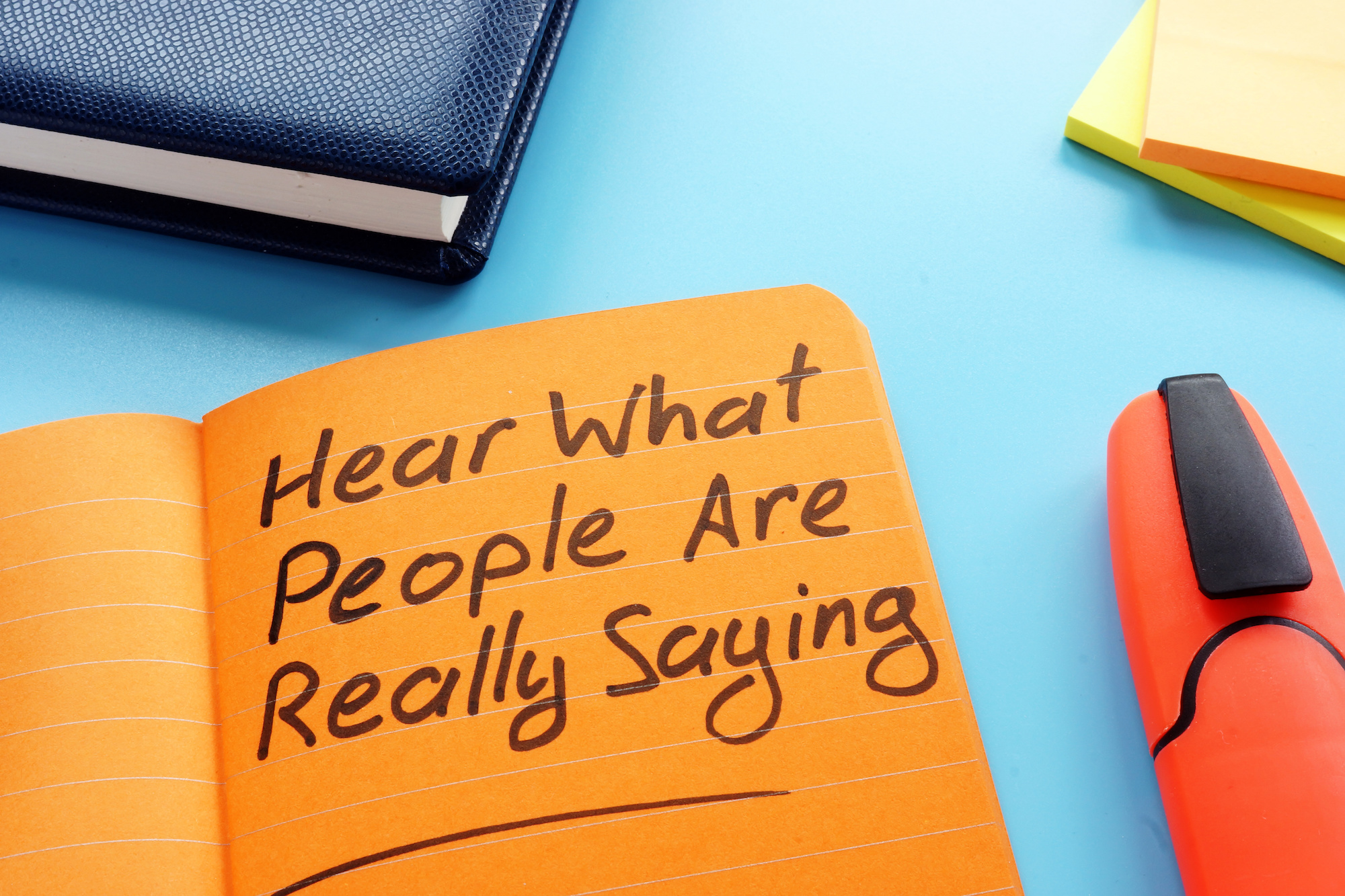 Orange notepad that reads "hear what people are really saying" next to a marker.