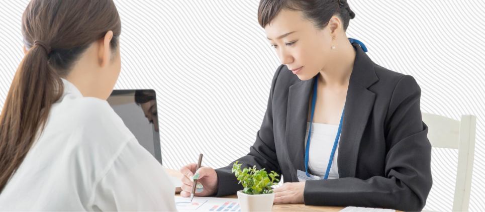 Two women sit at a desk going over a contract.