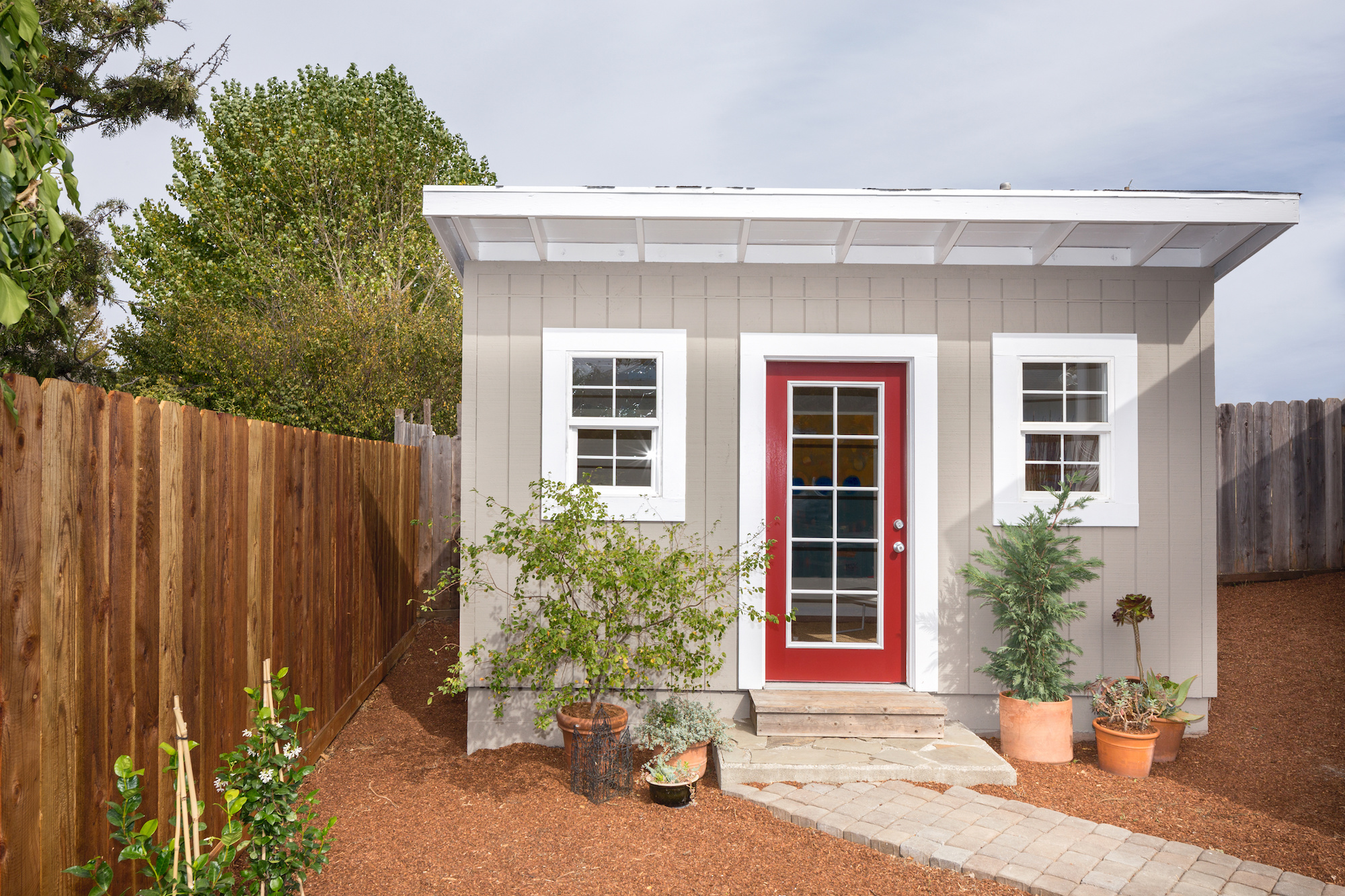 Small grey standalone bungalow with a red door and white trim.