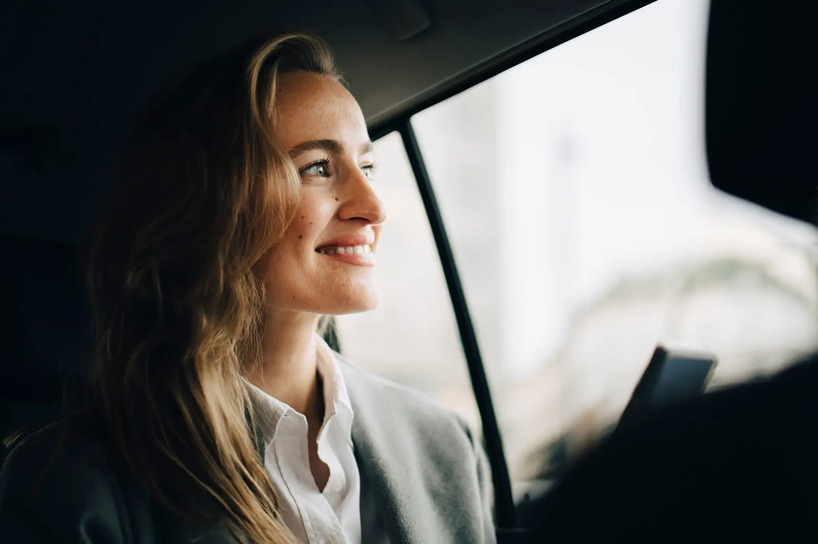 Eine selbstbewusste, lächelnde Unternehmerin, die im Taxi sitzt und durch das Fenster guckt.